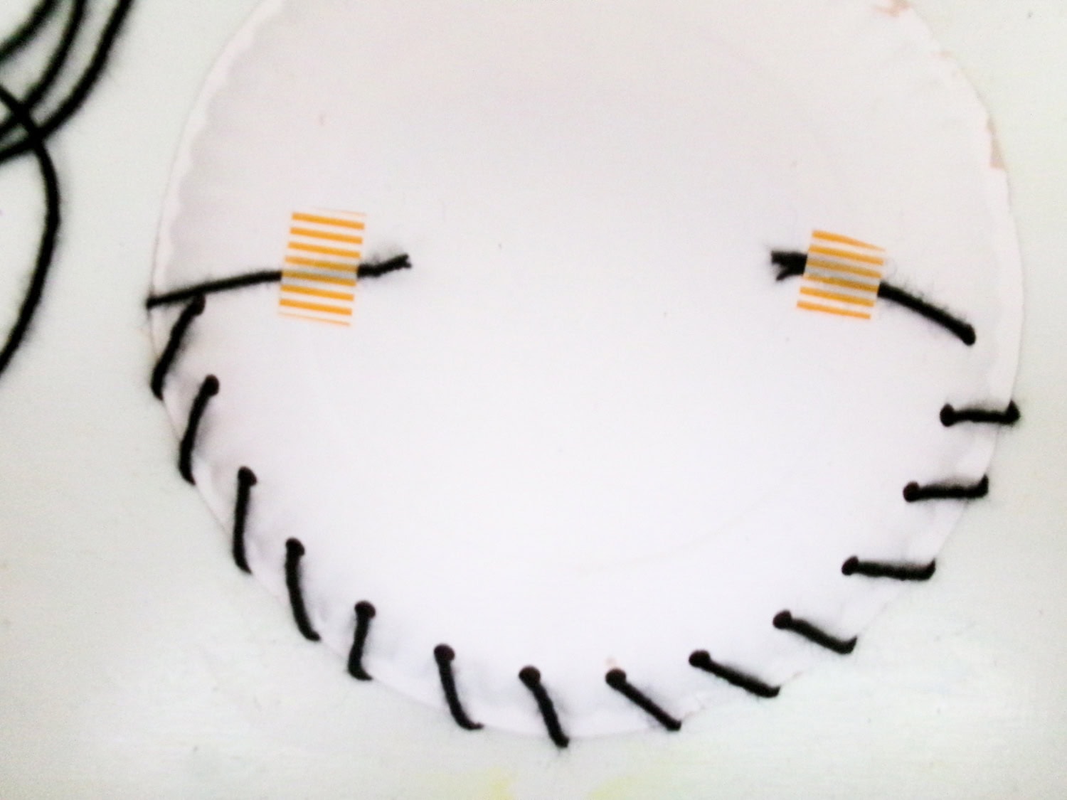 The black yarn threaded through the poles and taped to the back of the painted face for the Paper Plate Scarecrow Craft