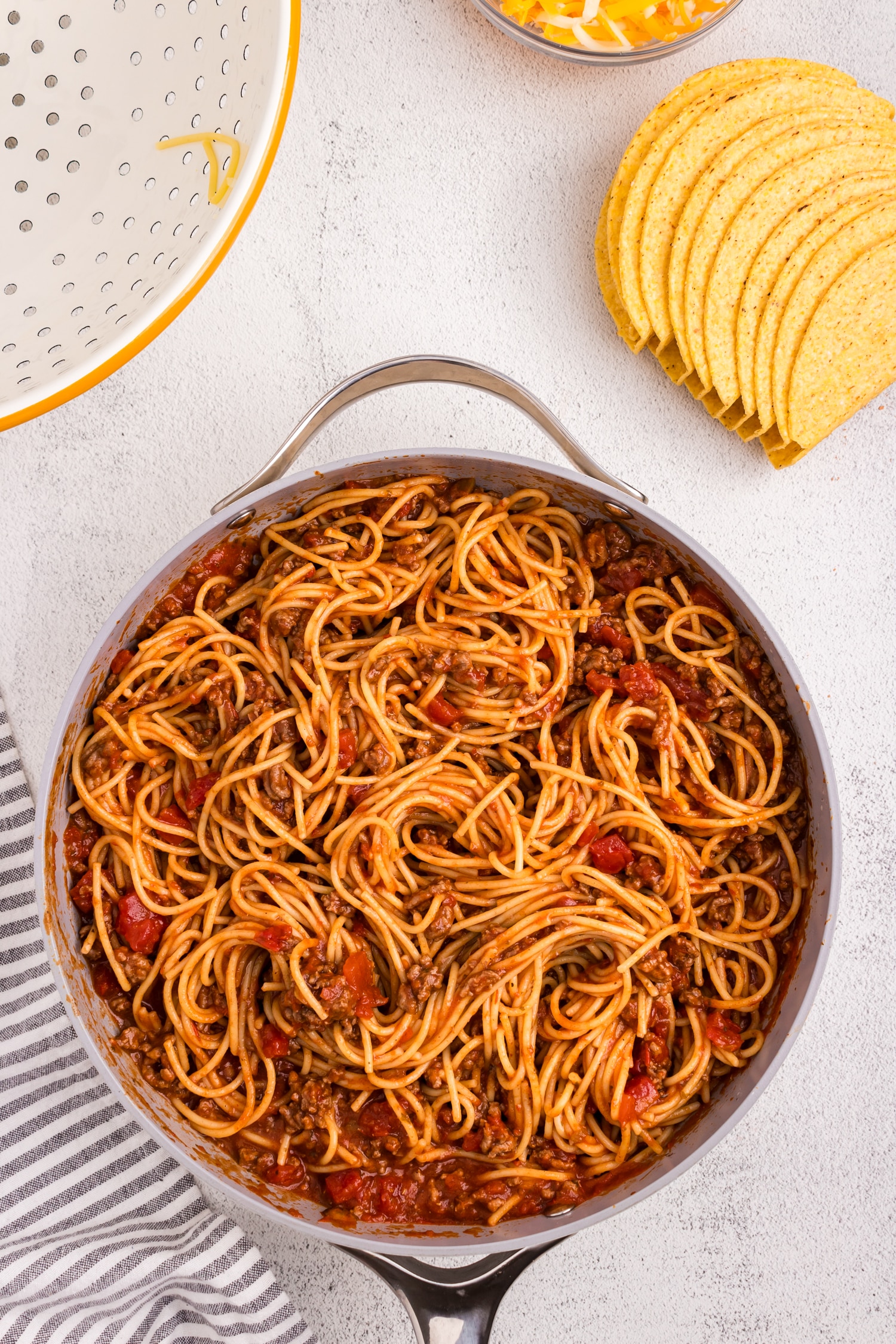 Adding spaghetti noodles to sauce mixture in skillet for Spaghetti Tacos