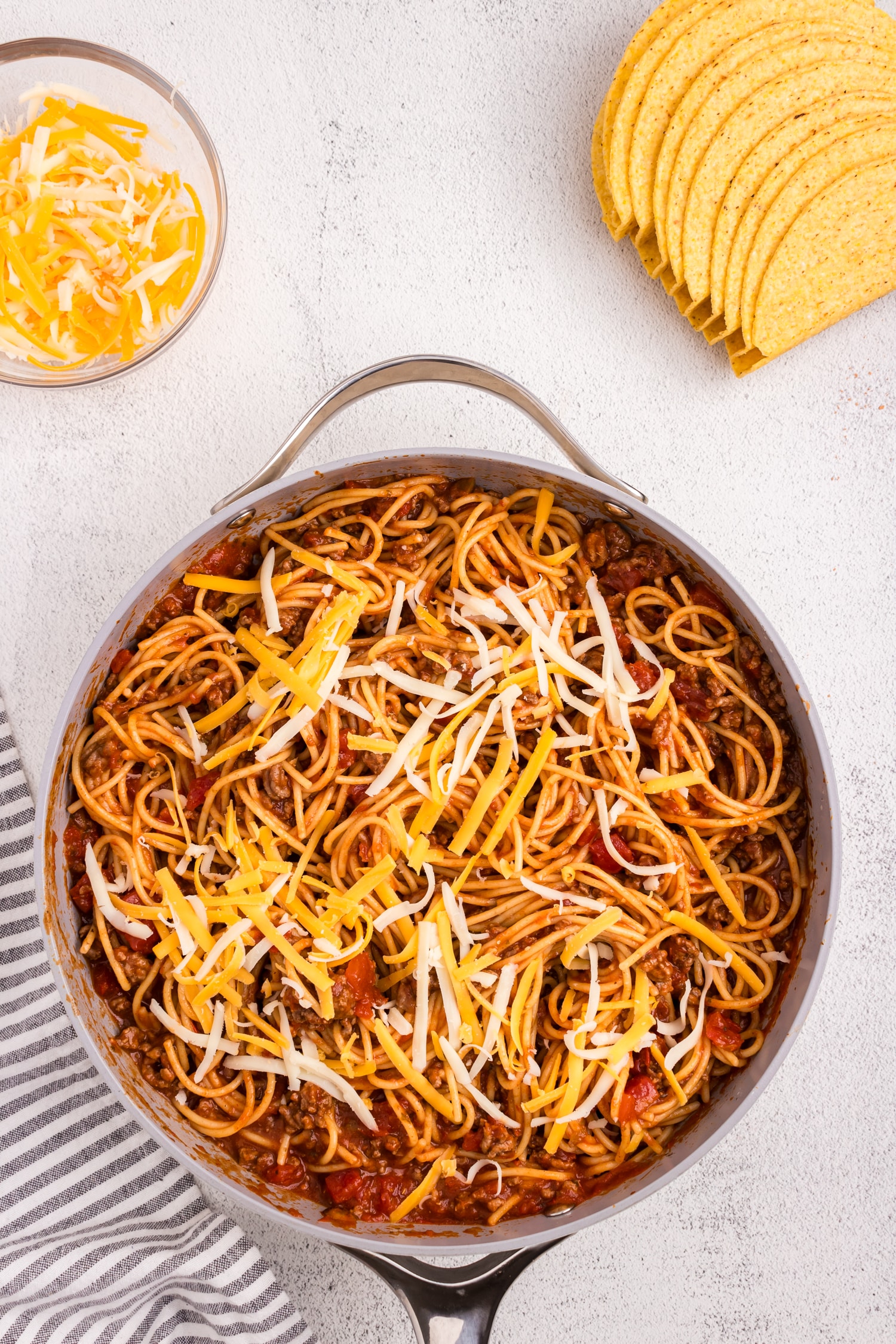 Spaghetti Tacos mixture in skillet topped with shredded cheese