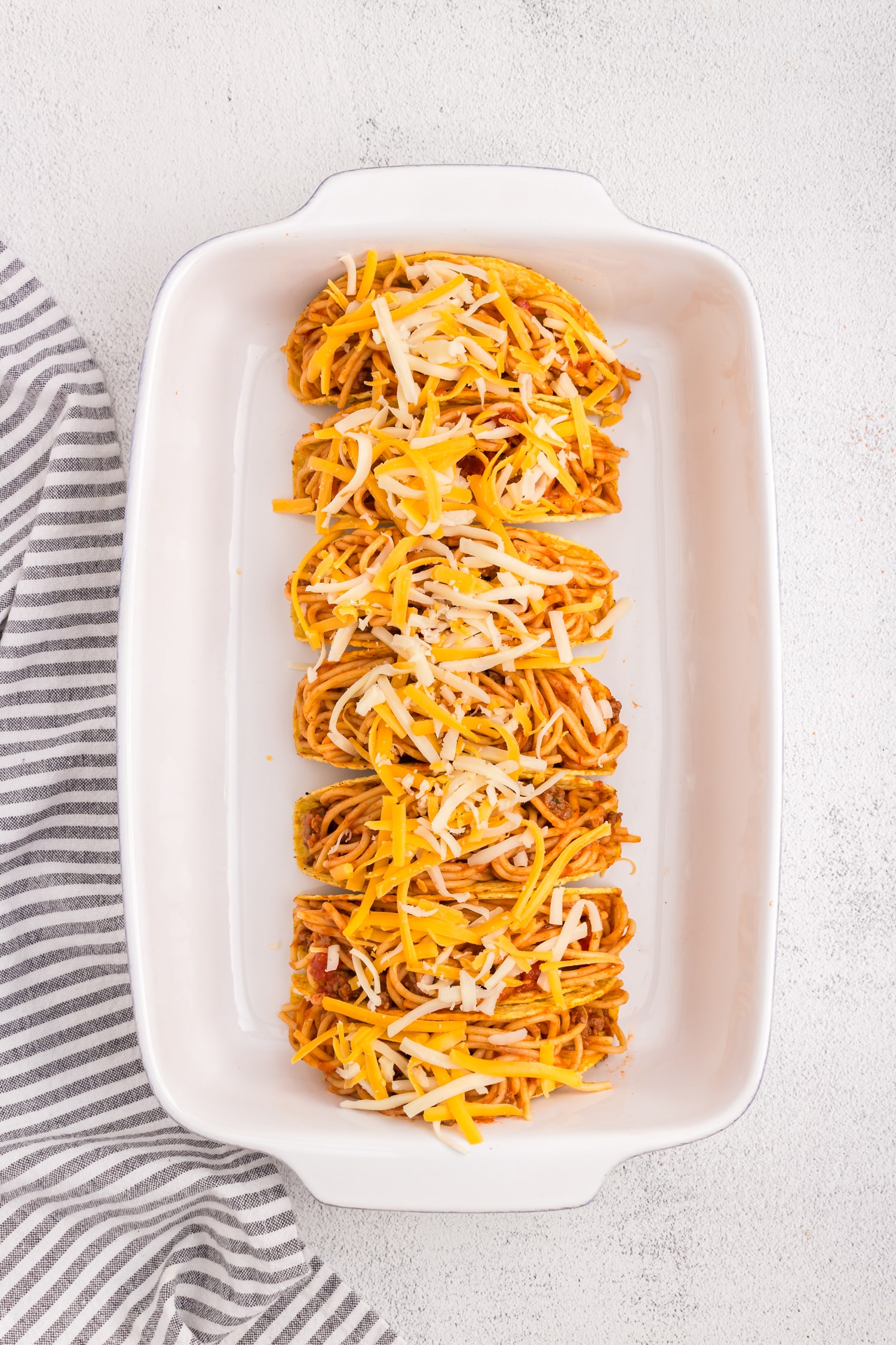 Topping the Spaghetti Tacos with shredded cheese in 9x13 baking pan