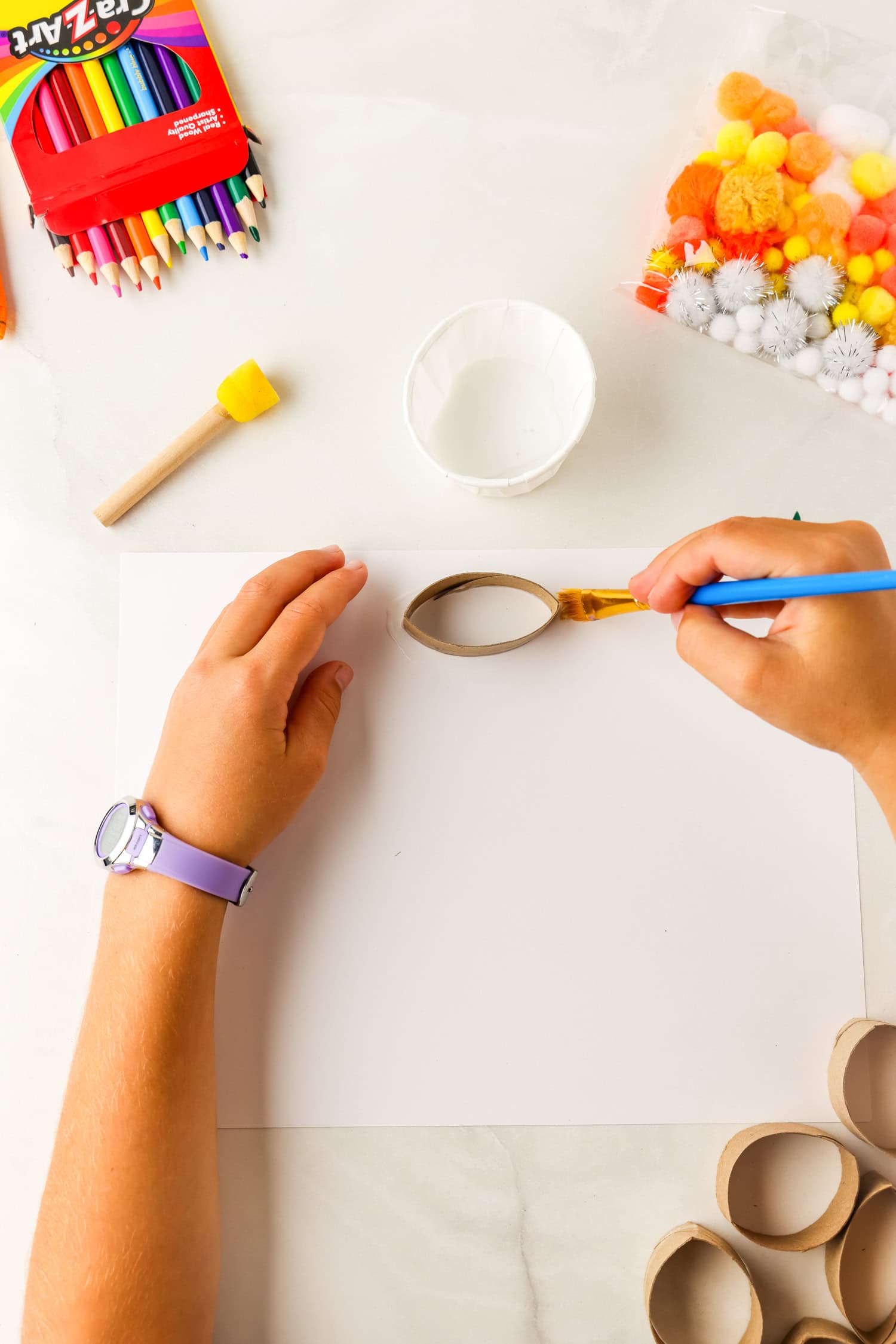Pressing down toilet paper tube on painted on glue for Butterfly Life Cycle Craft