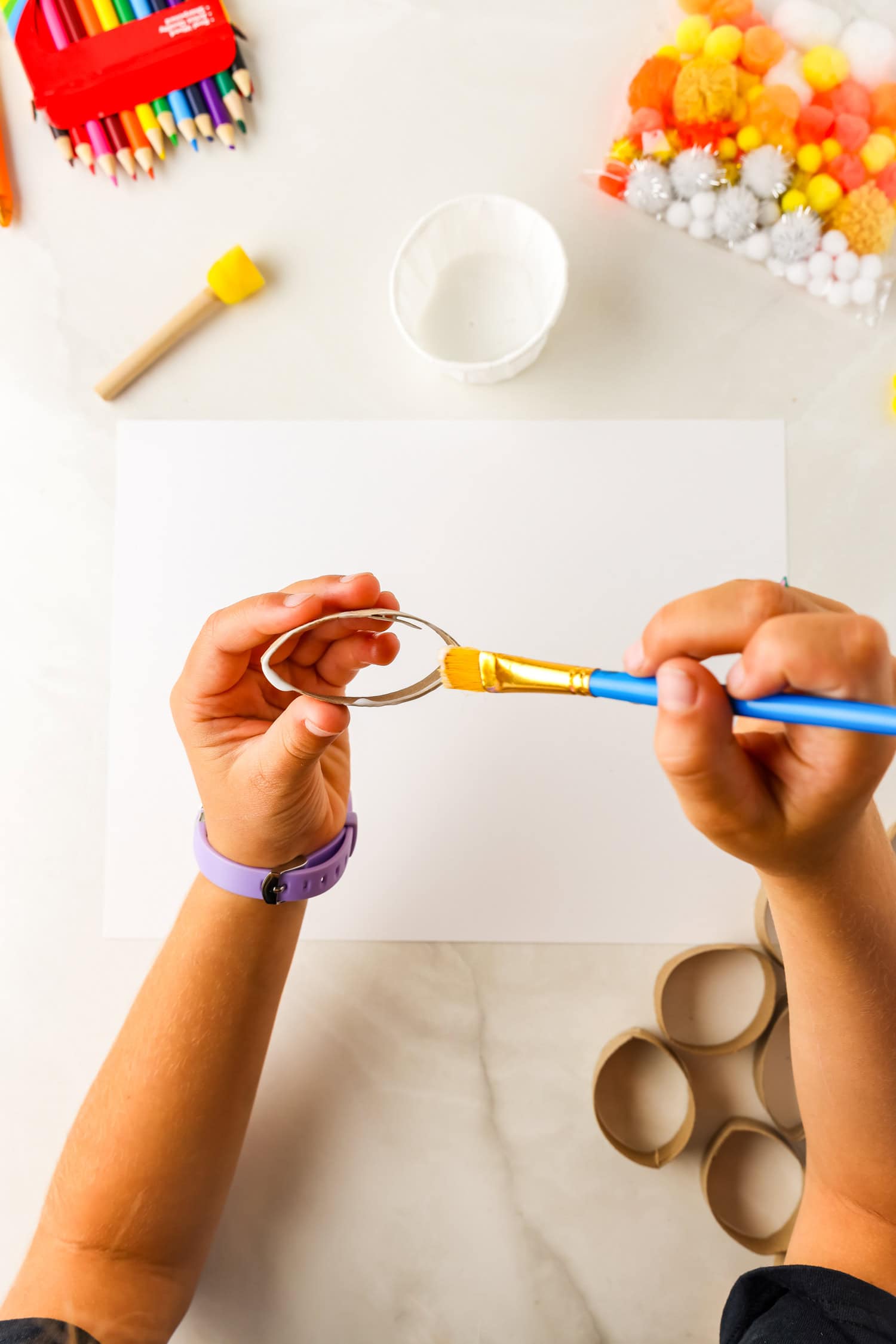 Painting school glue onto edges of toilet paper tubes for Butterfly Life Cycle Craft