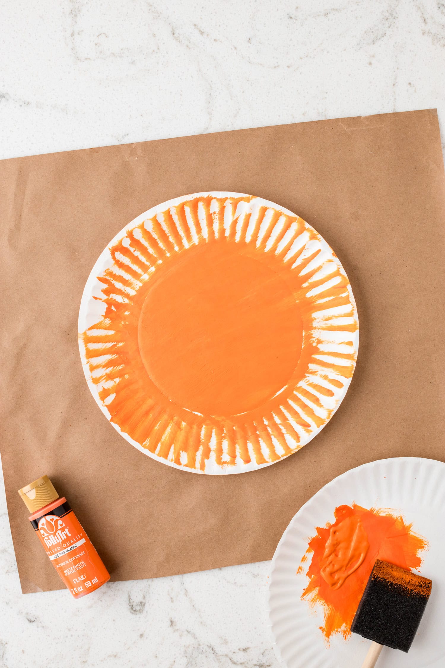 Painting a white paper plate orange for the Paper Plate Pumpkin Craft