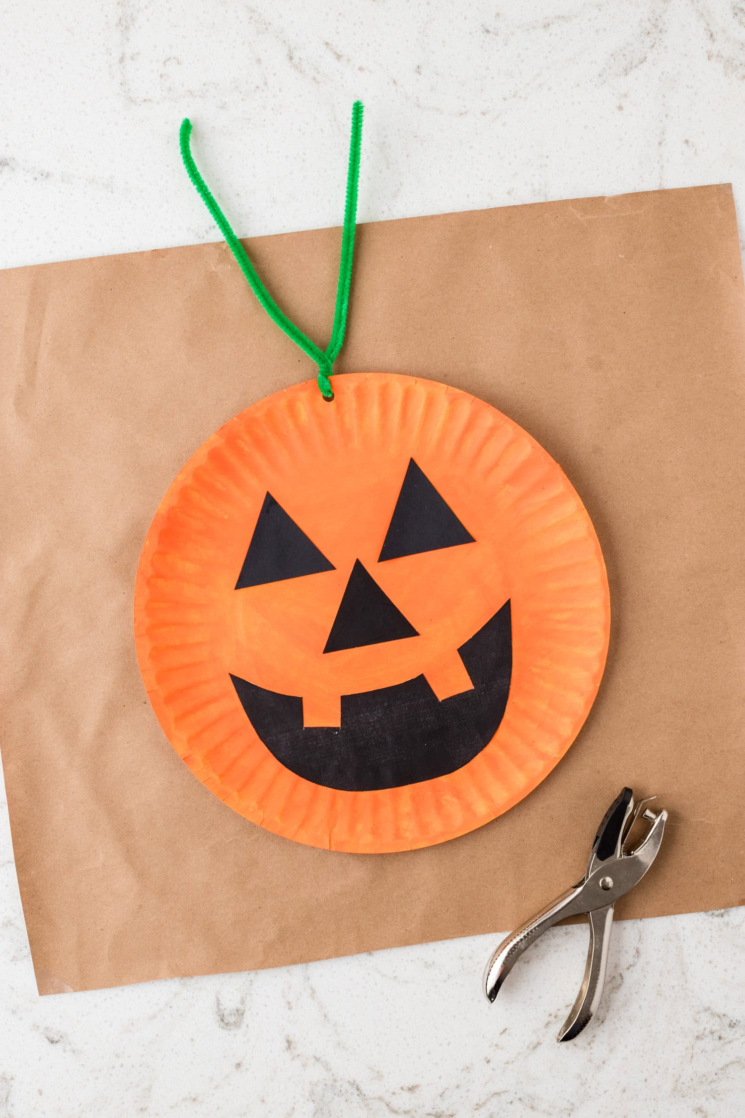 Using a hole punch to create one hole for the green pipe cleaner to twist into for the Paper Plate Pumpkin Craft