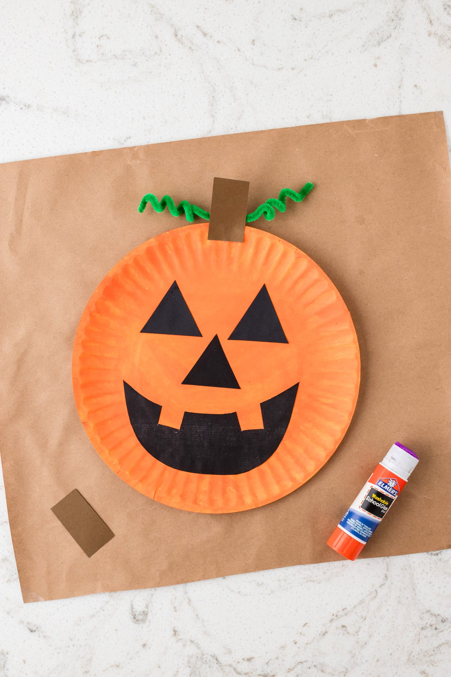 Using a glue stick to glue a brown stem to the top of the Paper Plate Pumpkin Craft