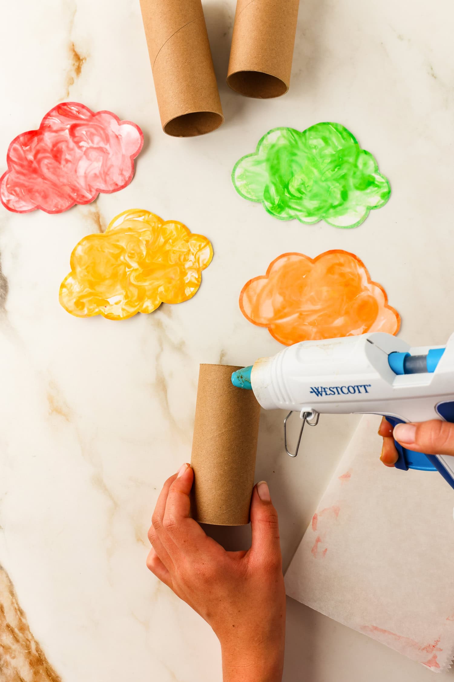 Using a glue gun to add hot glue on the toilet paper roll to affix the tree top for the Toilet Paper Roll Fall Tree Craft