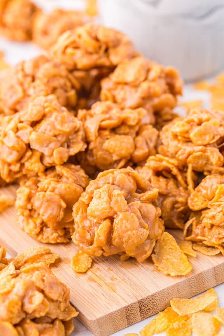 A Pile of Cornflake Cookies Piled up on top of one another displayed on a wooden cutting board.