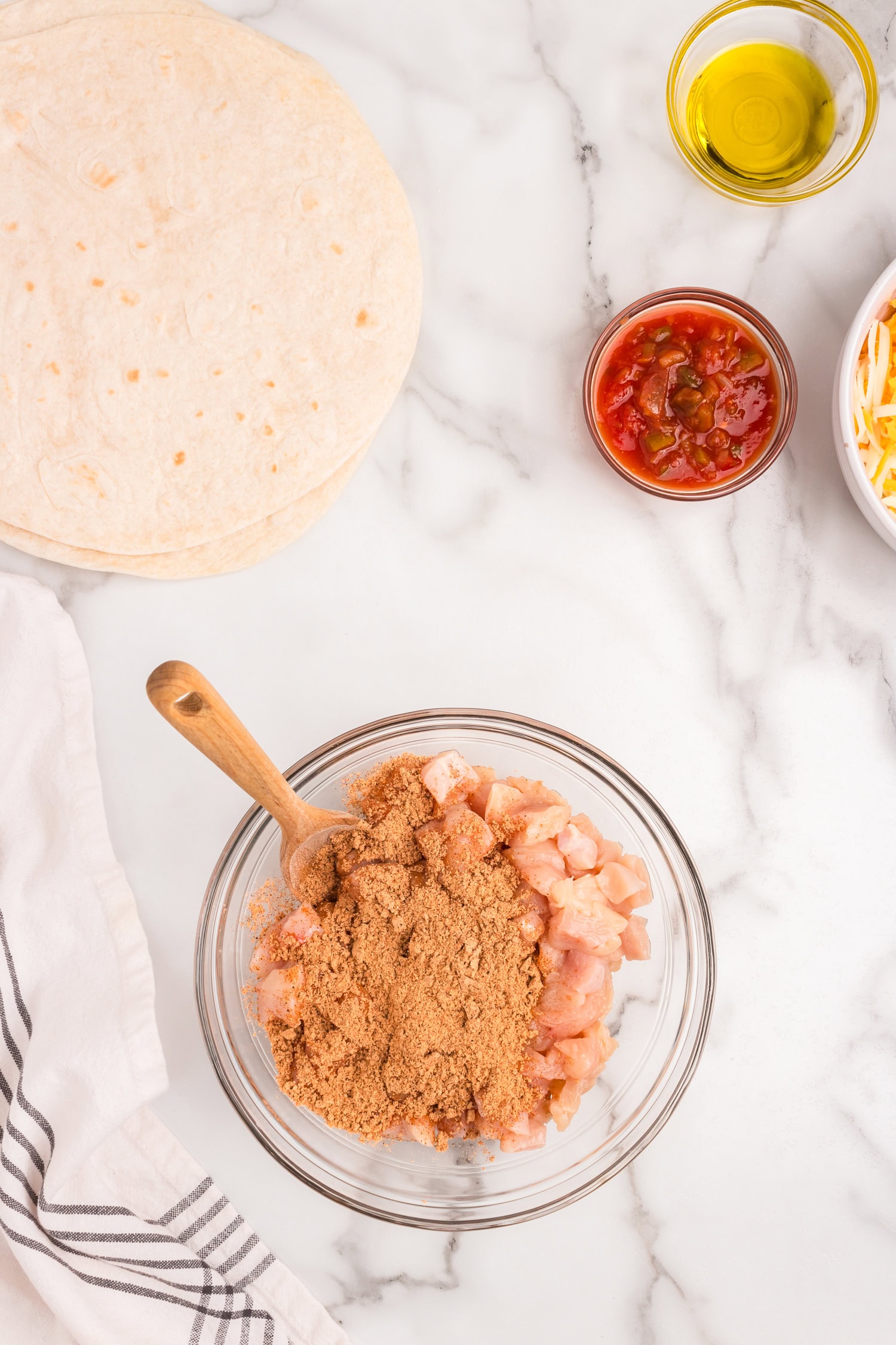 Tossing cubed chicken breasts and taco seasoning in glass mixing bowl for Chicken Quesadilla recipe