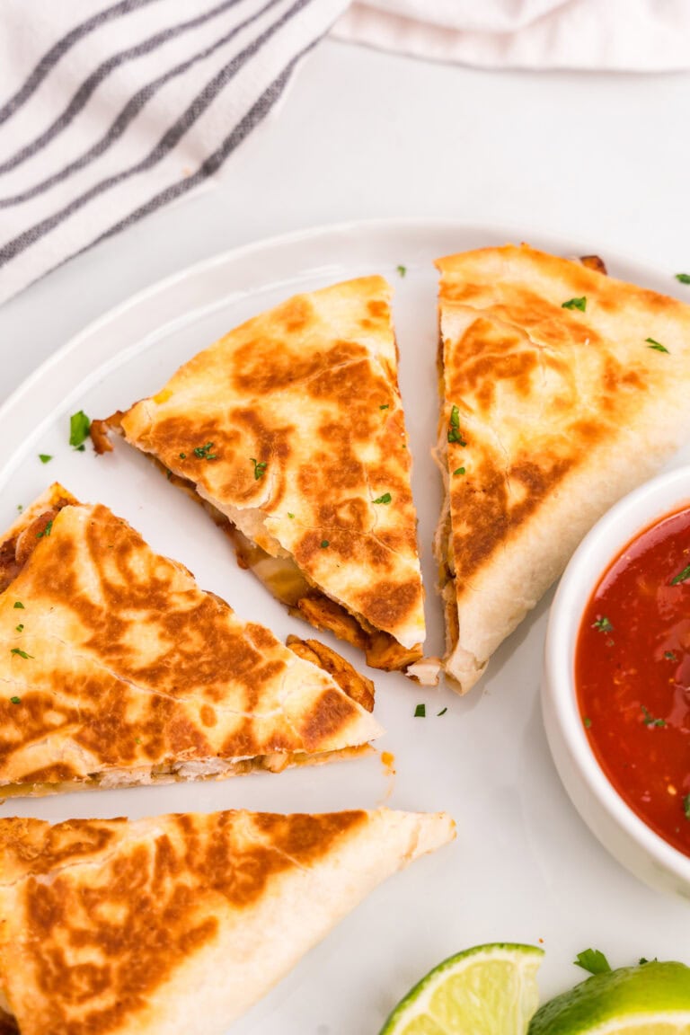 Chicken Quesadillas cut into triangle slices on white plate with salsa in bowl
