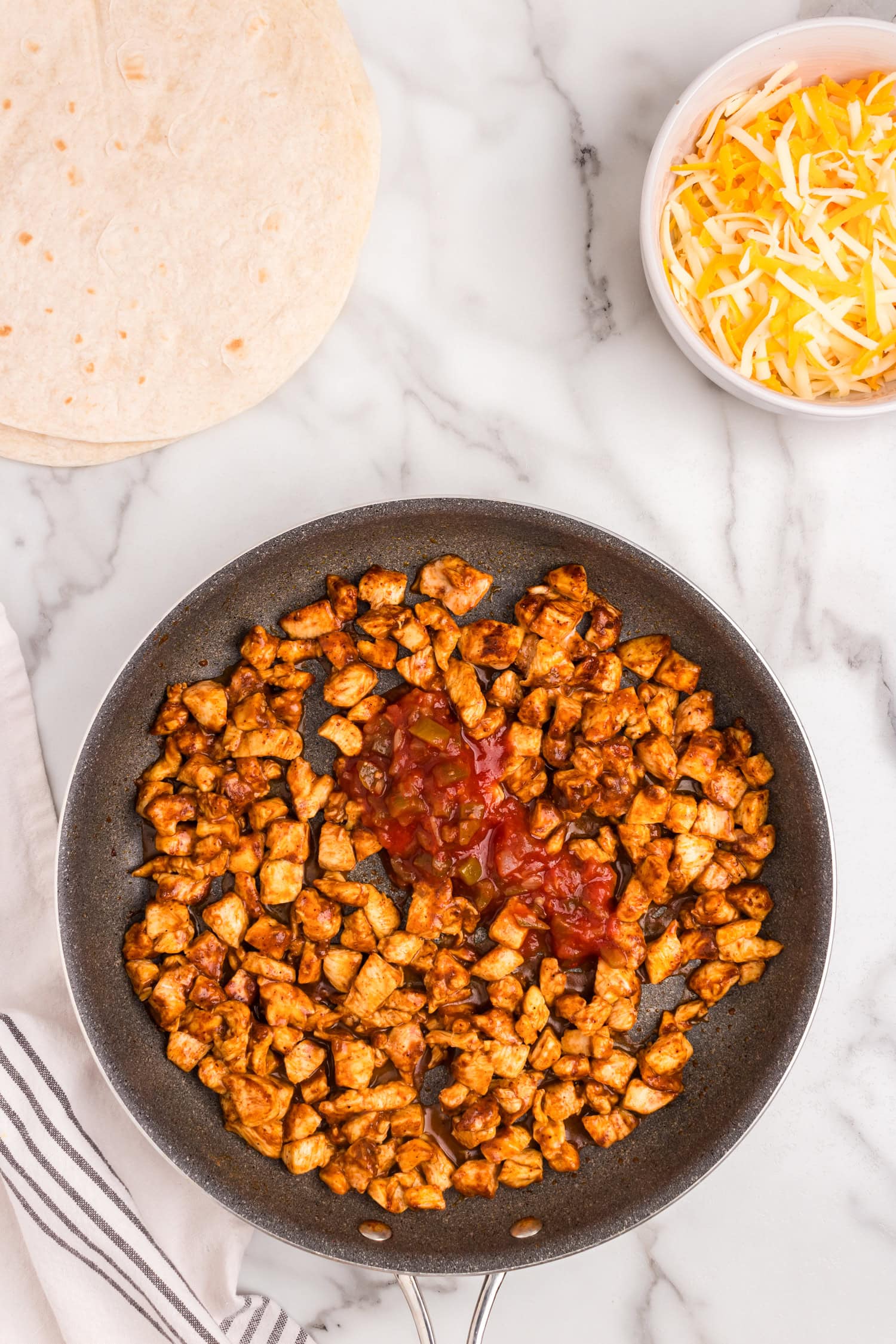 Cooking seasoned chicken in stovetop skillet with olive oil and salsa for Cubed chicken coated in taco seasoning in small mixing bowl for Chicken Quesadilla recipe