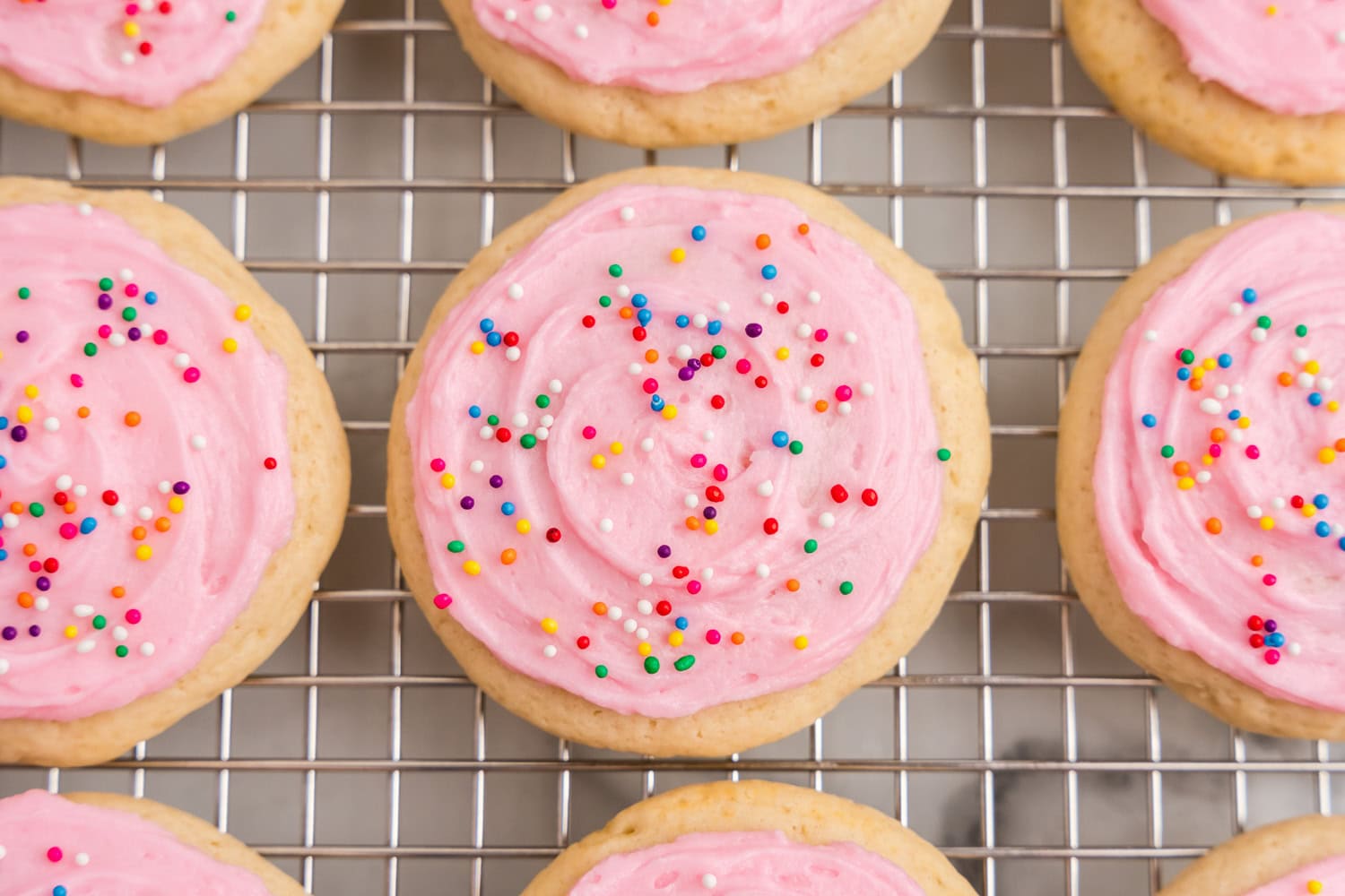 Frosted Sour Cream Cookies topped with colorful sprinkles on cooling rack