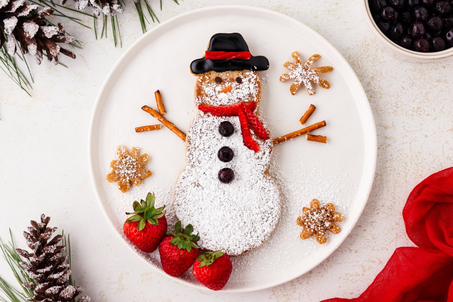 Completed snowman pancakes, strawberries and pancake snowflakes on a white plate.