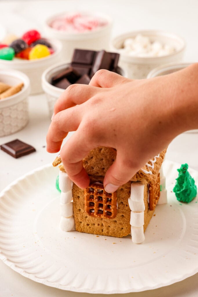 Hand putting square pretzel onto the ginger bread house.