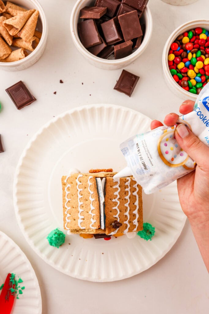 Overhead picture of icing being squeezed onto the roof of the gingerbread house in a pattern.