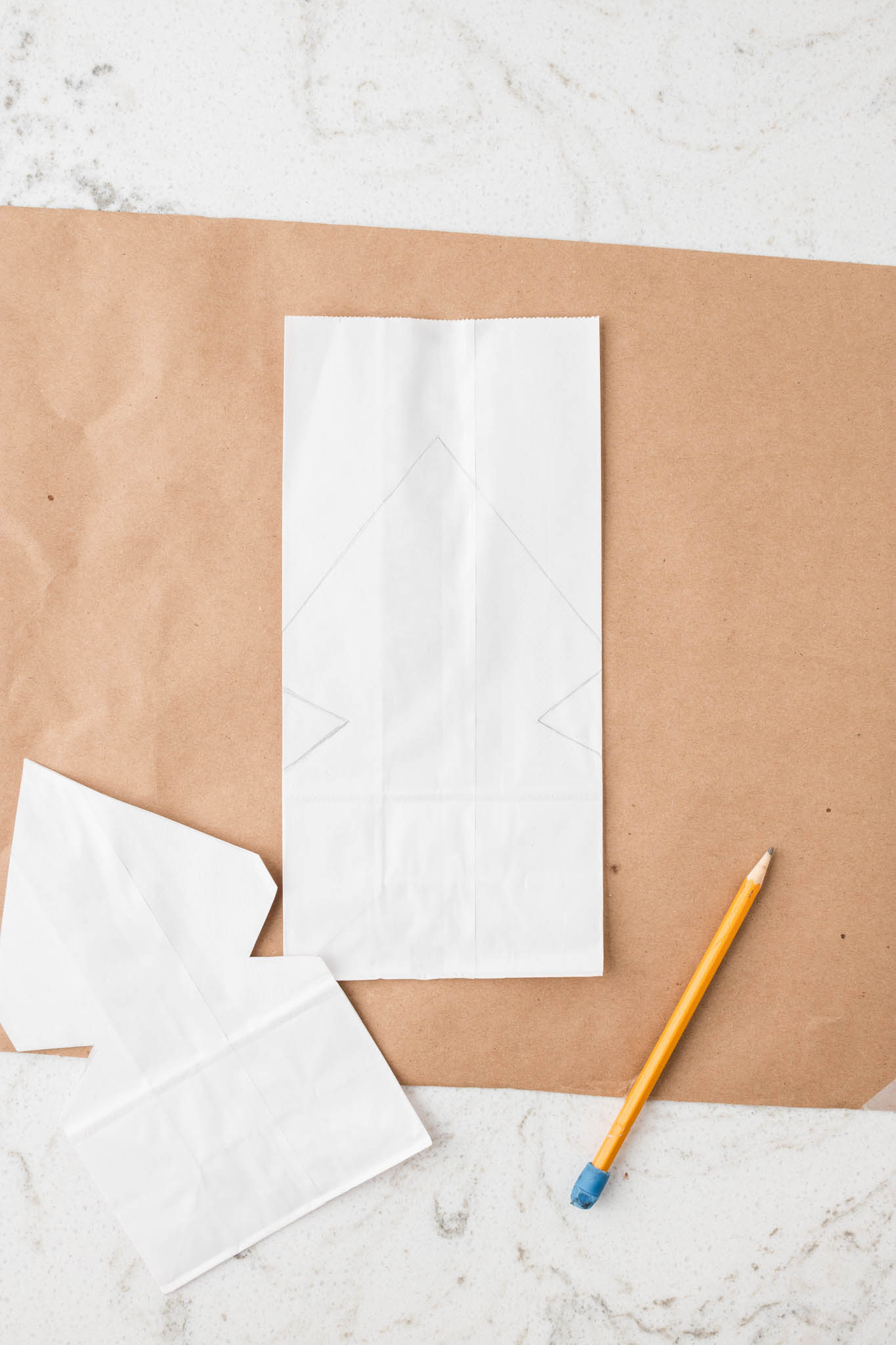 Overhead picture of one uncut and one cut paper bag and a pencil.