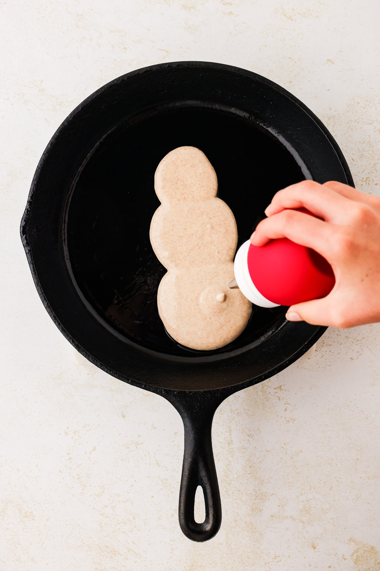 Hand squeezing frosting bulb to make snowmans bottom.
