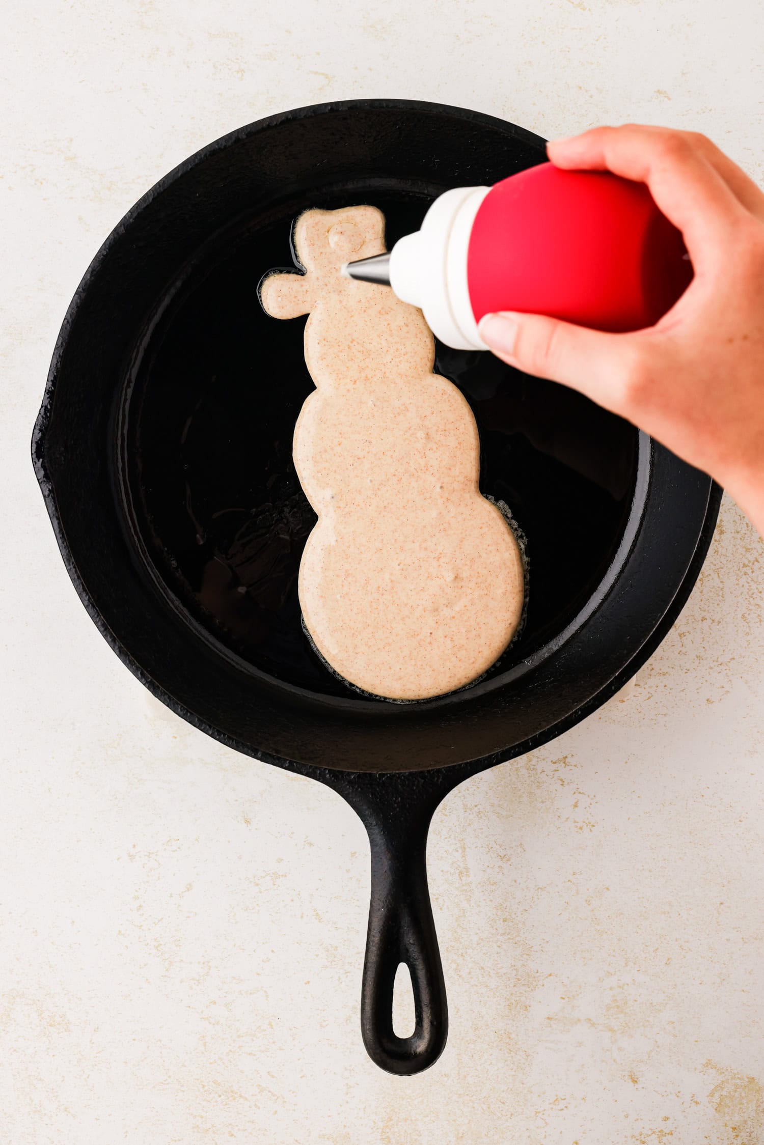 Hand squeezing frosting bulb to fill in the snowmans hat.