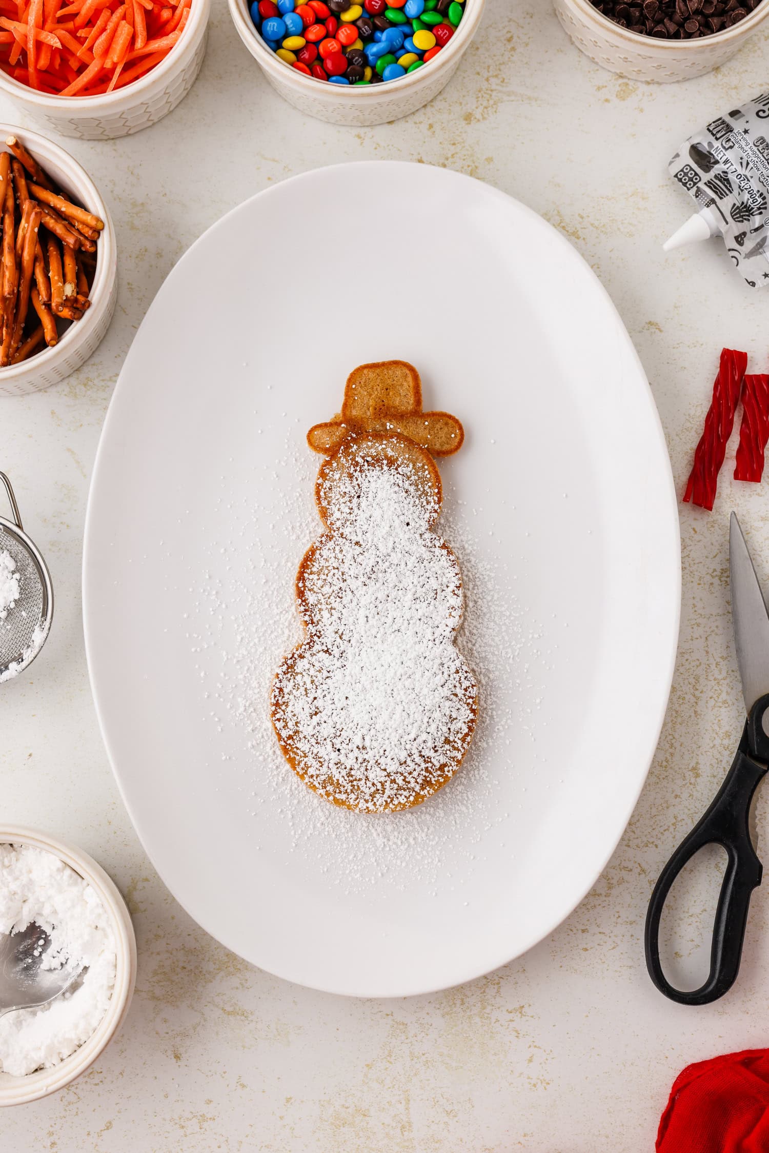Snowman pancake covered in powdered sugar on a white oval plate.