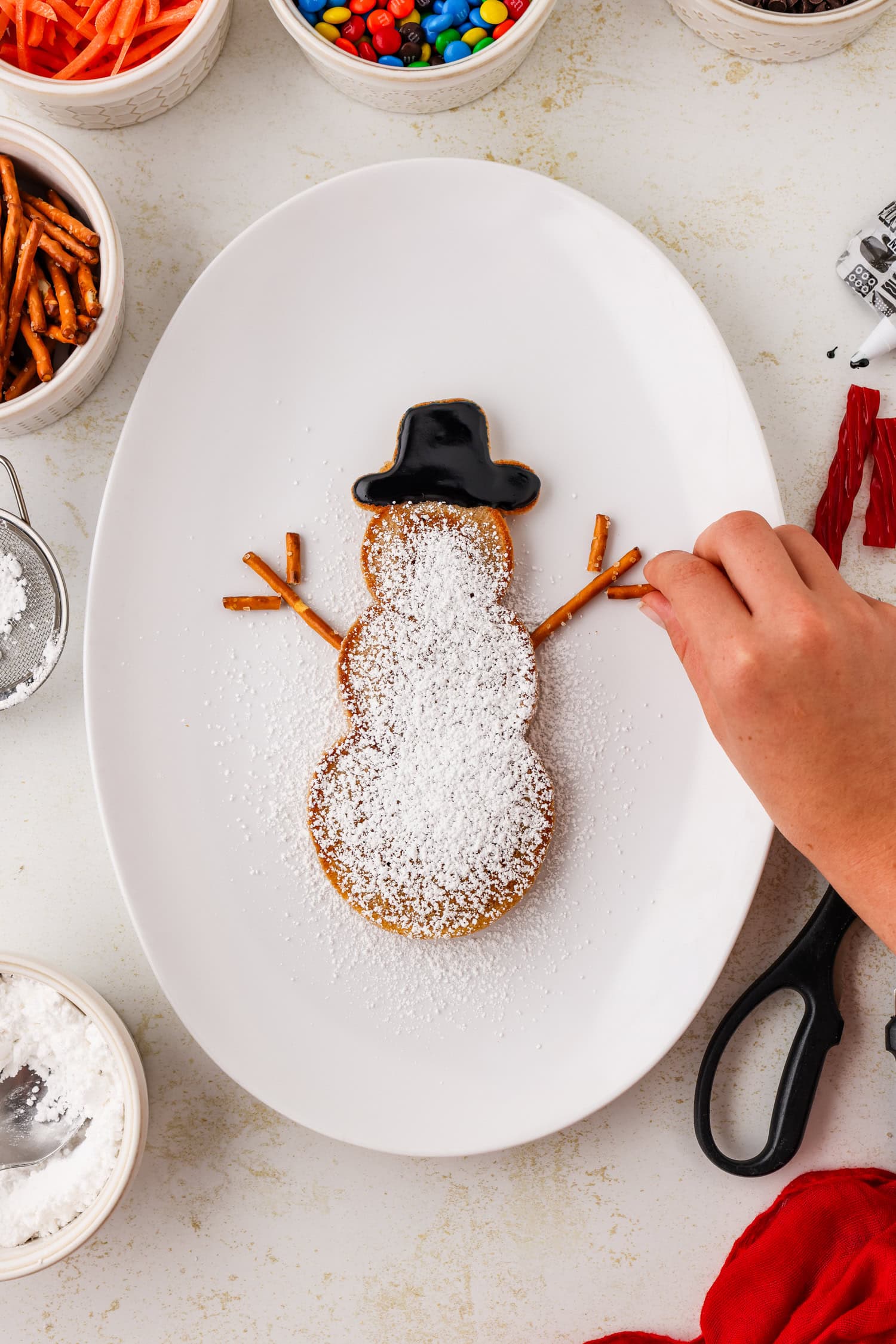 Snowman pancake with pretzel arms being put on it.