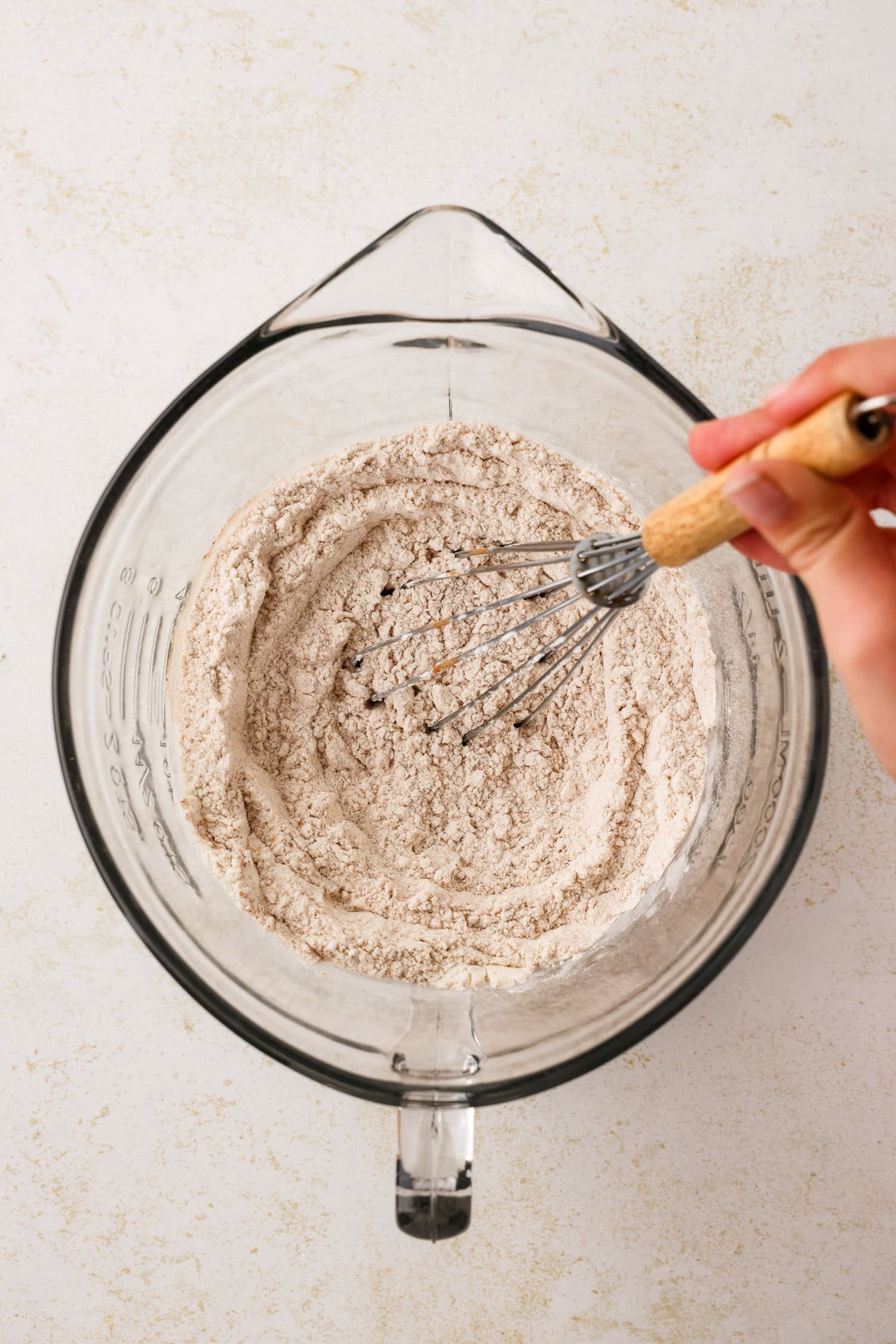 Glass measuring bowl with dry snowman pancake ingredients being mixed with a whisk.