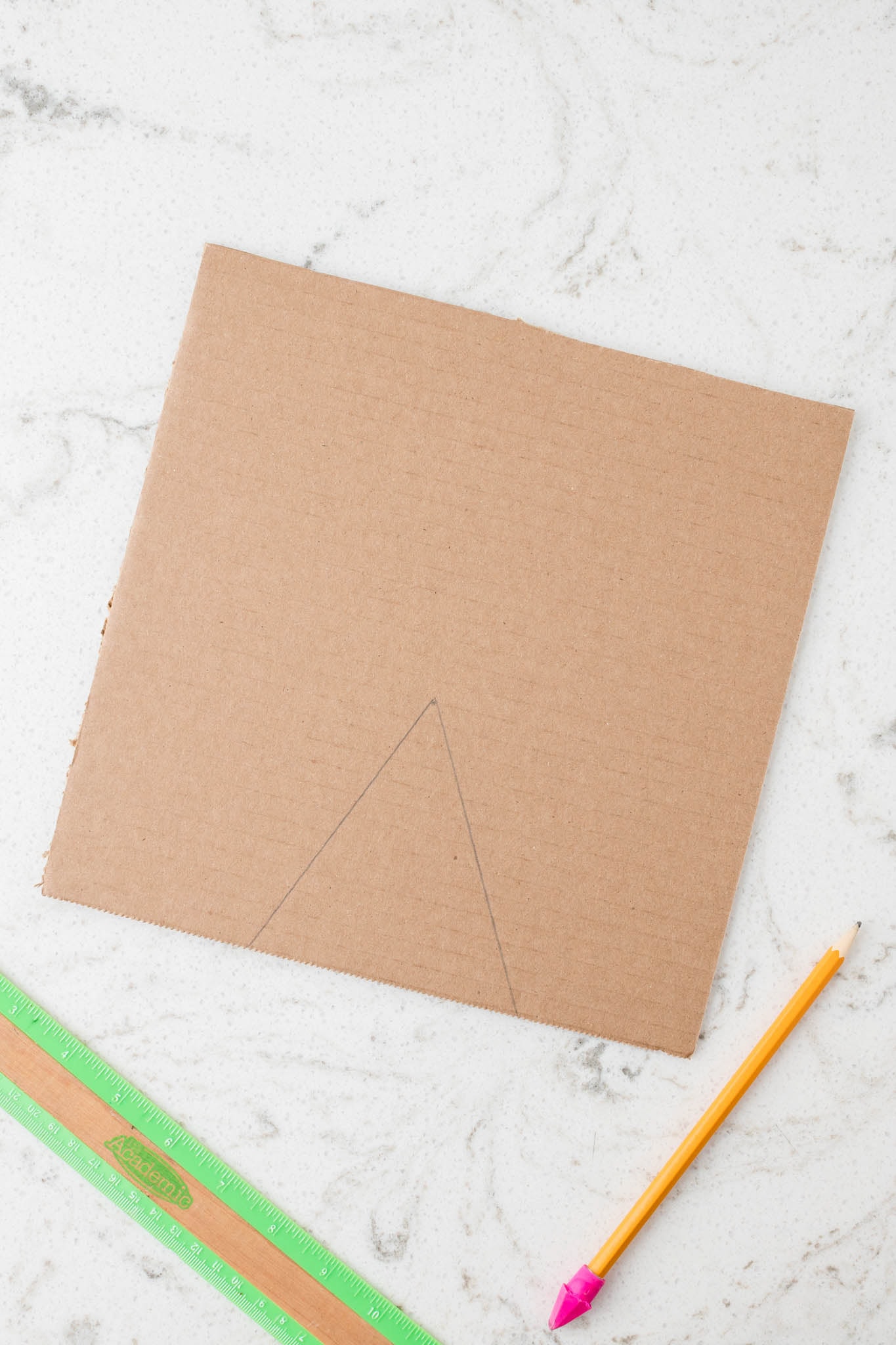 Overhead picture of cardboard square with a triangle penciled on it.
