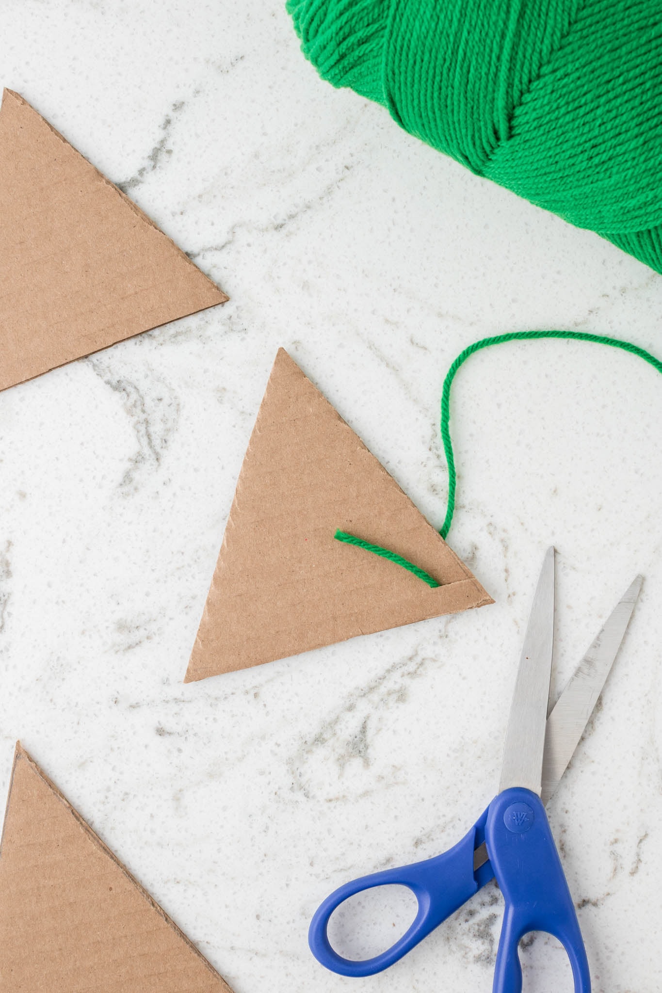 Overhead picture of a cardboard triangle with a small hole with a piece of yarn sticking through it.