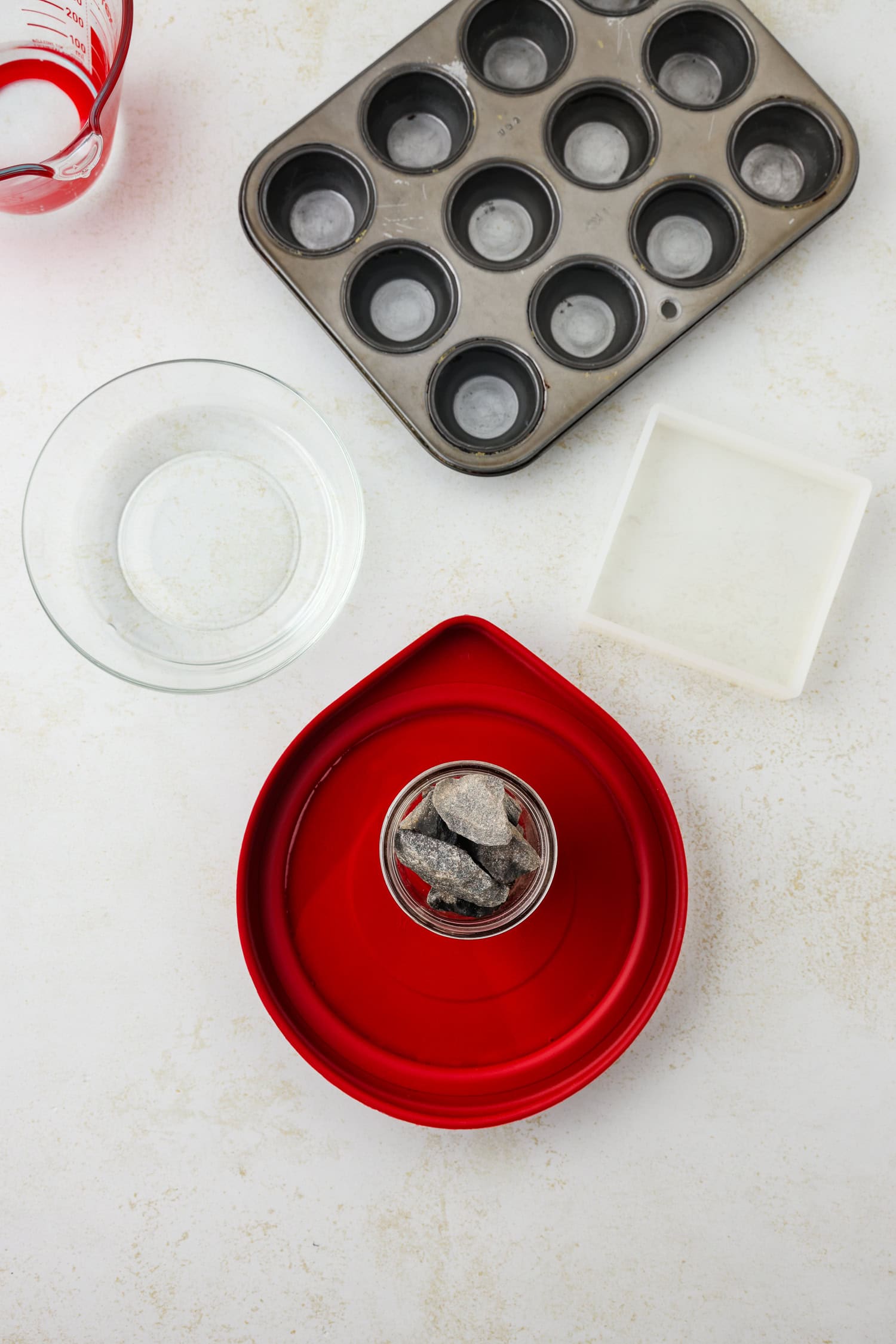 Overhead picture of muffin tin, a bowl, square container and red lid with a jar on it.