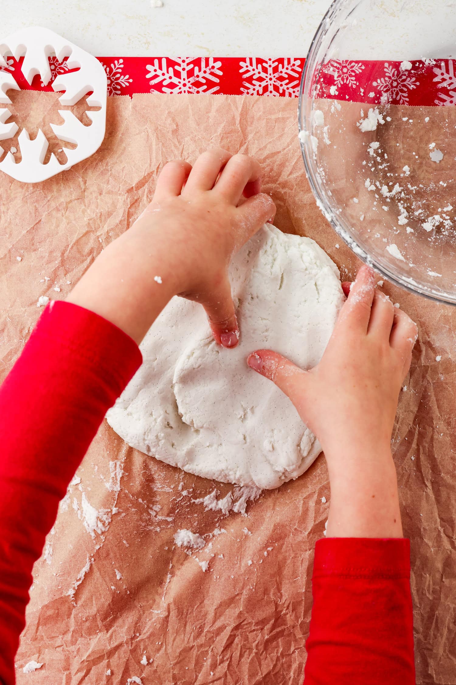 Overhead picture of hands pressing thumbs into snow dough on parchment paper.