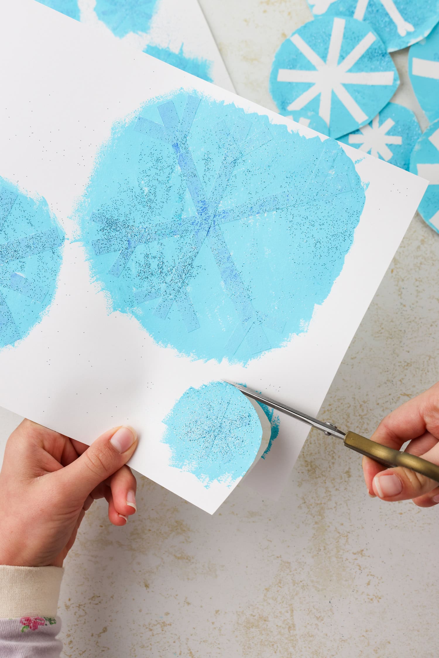Overhead picture of a hand cutting out the circular snowflakes.