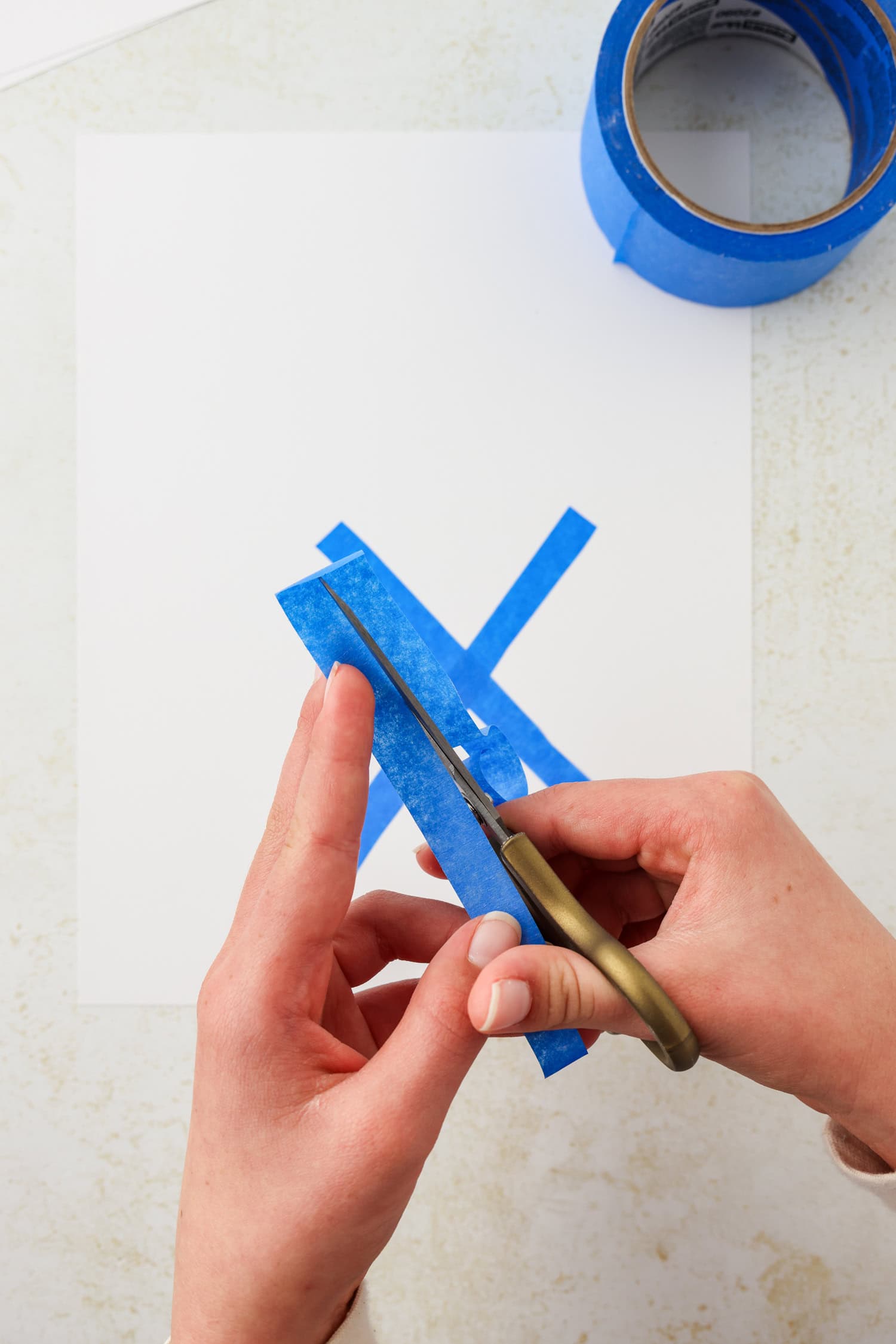 Overhead picture of blue painters tape being placed on cardstock paper in pattern of a snowflake.