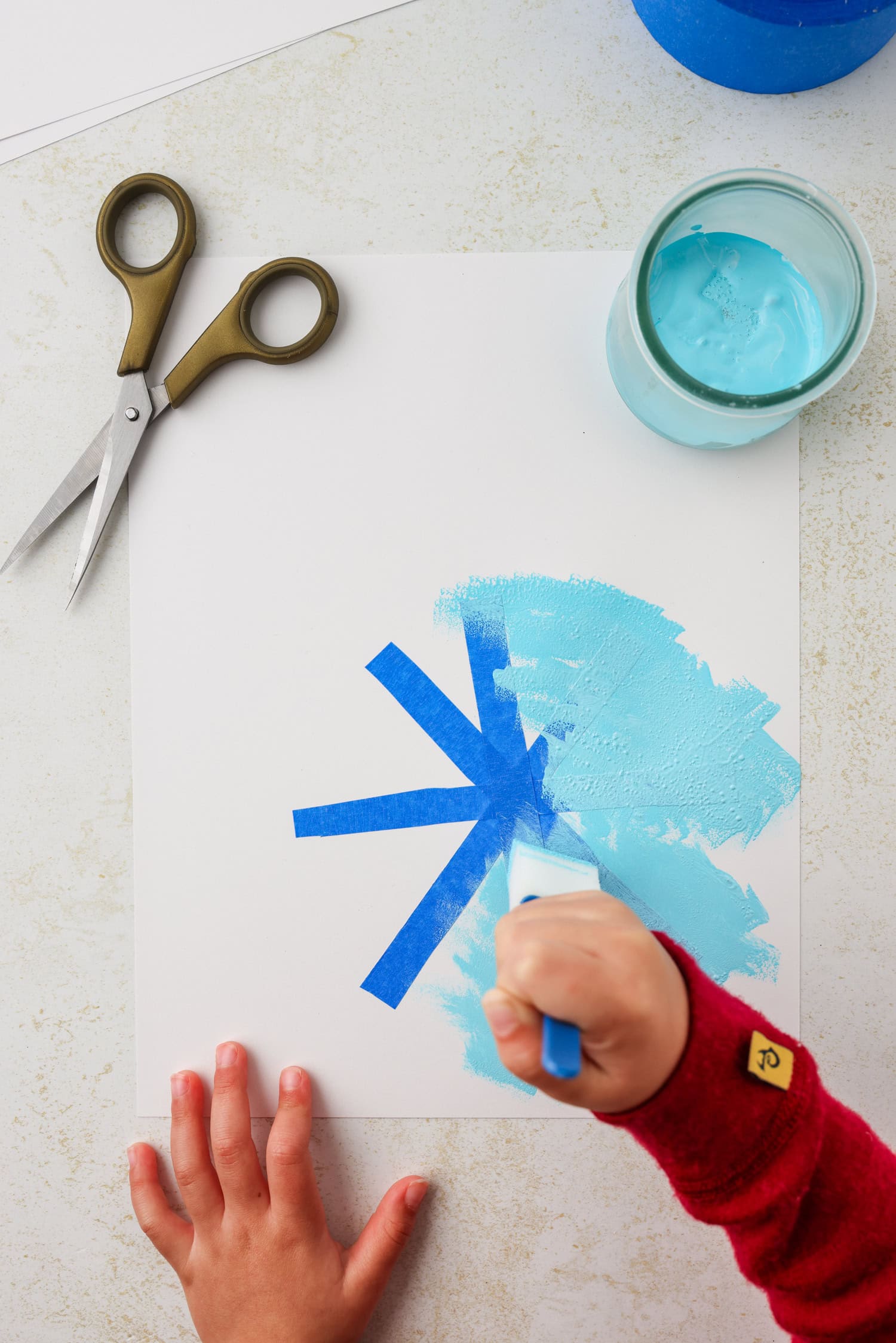Overhead picture of hand painting blue paint over painters tape.
