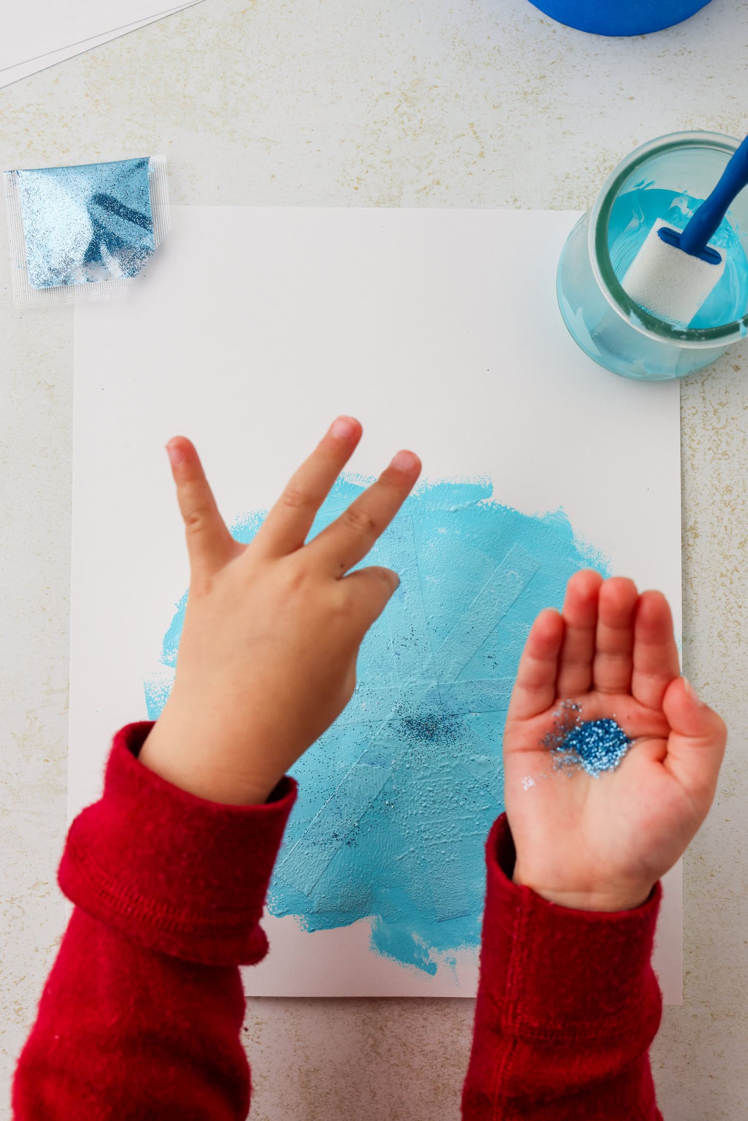Overhead picture of hand sprinkling glitter onto the paint.