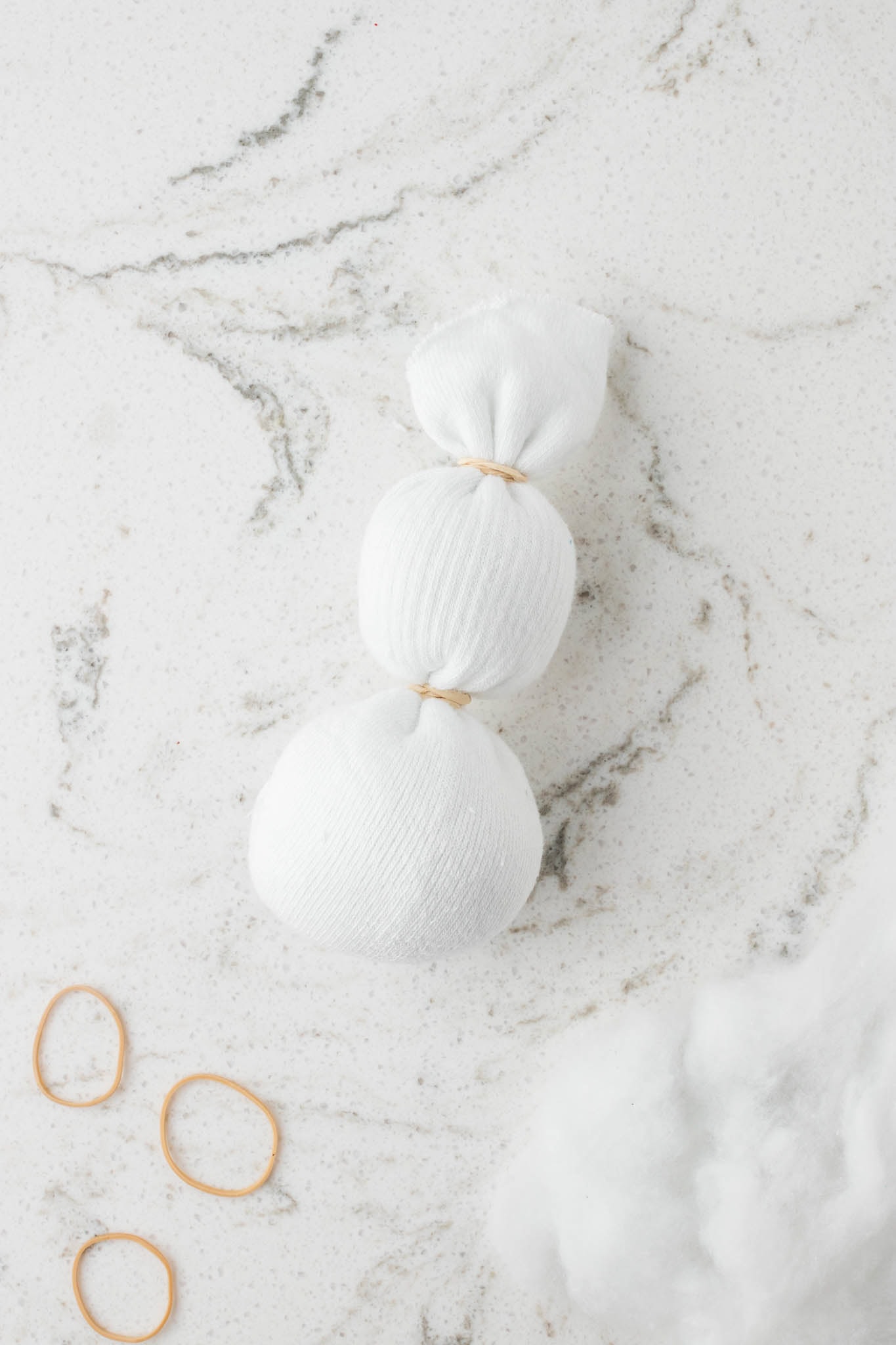 Picture of white crew sock filled with polyfil and rubber bands around 2 portions to make snowman shape