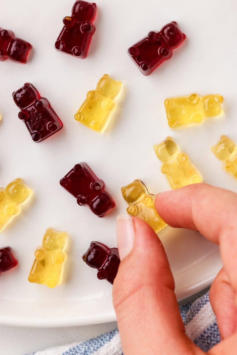 Picture of homemade gummy bears spread out on a plate with a hand grabbing one.