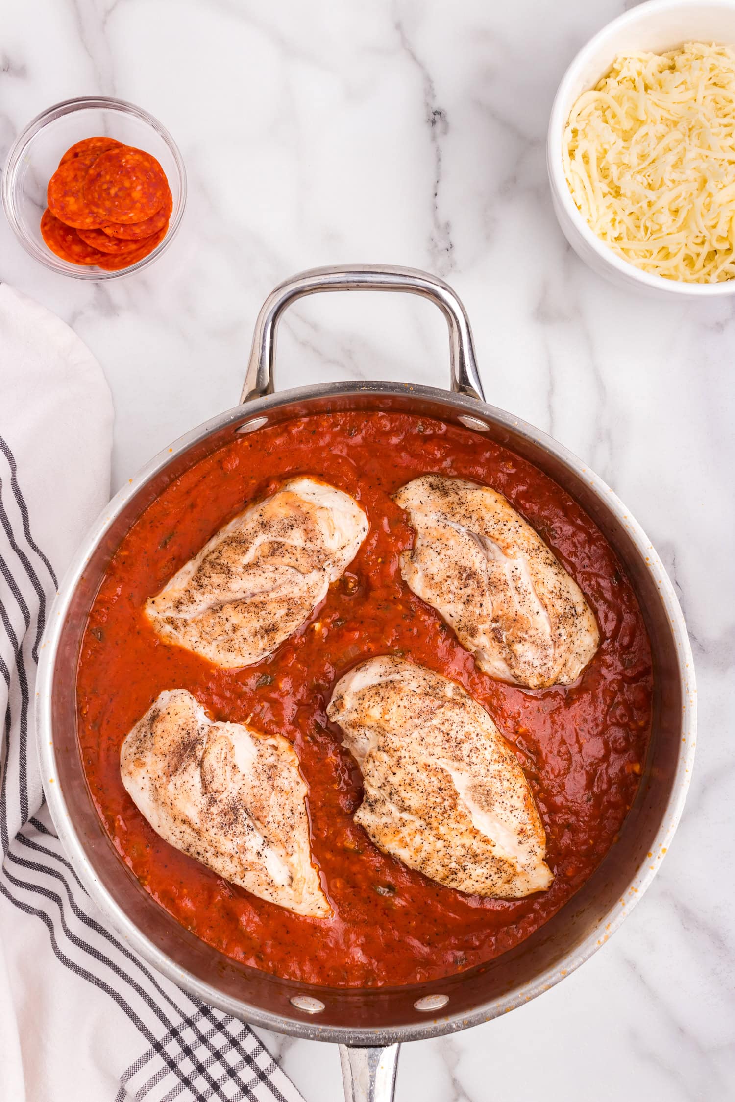 Overhead picture of cooked chicken breast in pizza sauce.