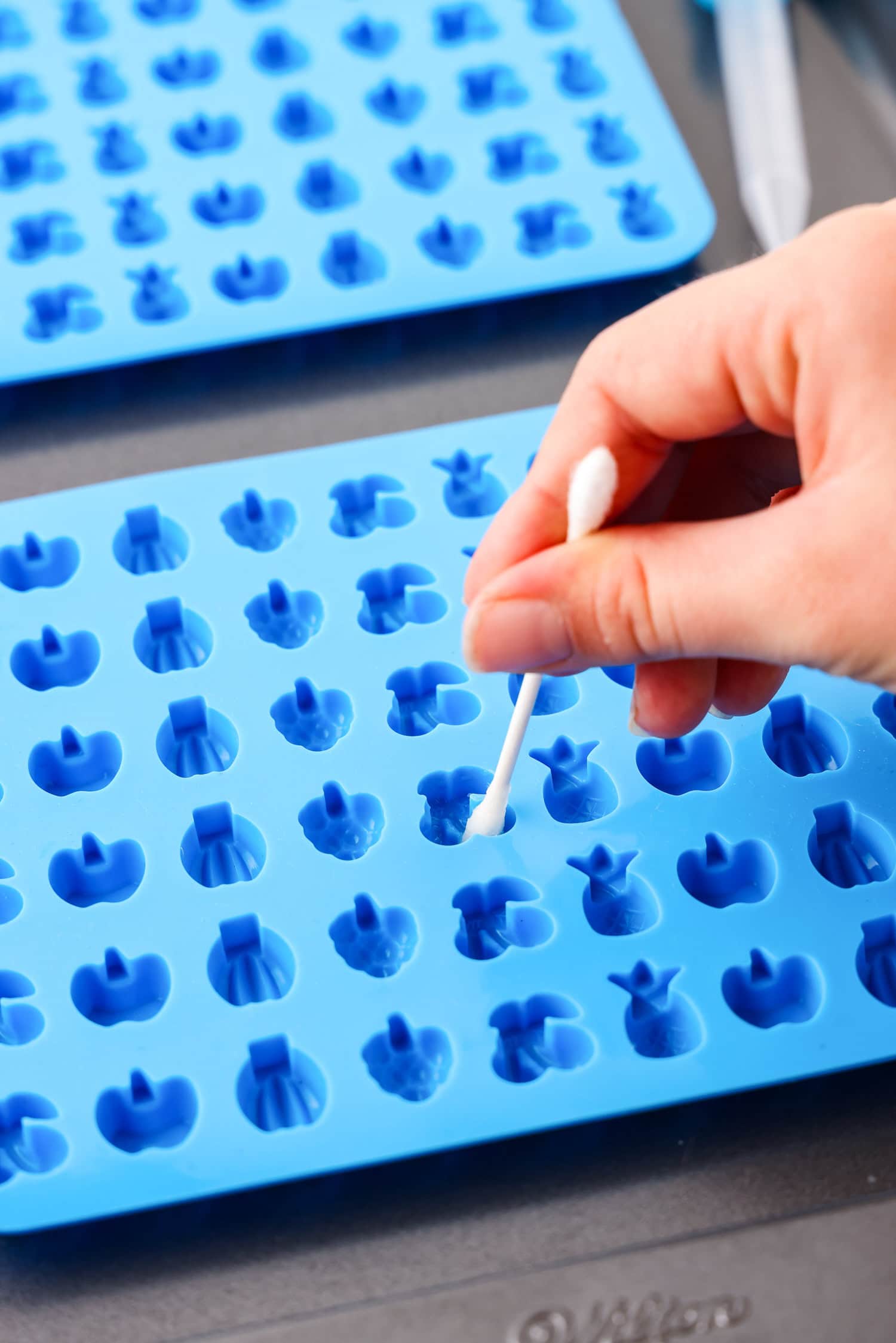 Hand using q tip inside fruit snack molds.