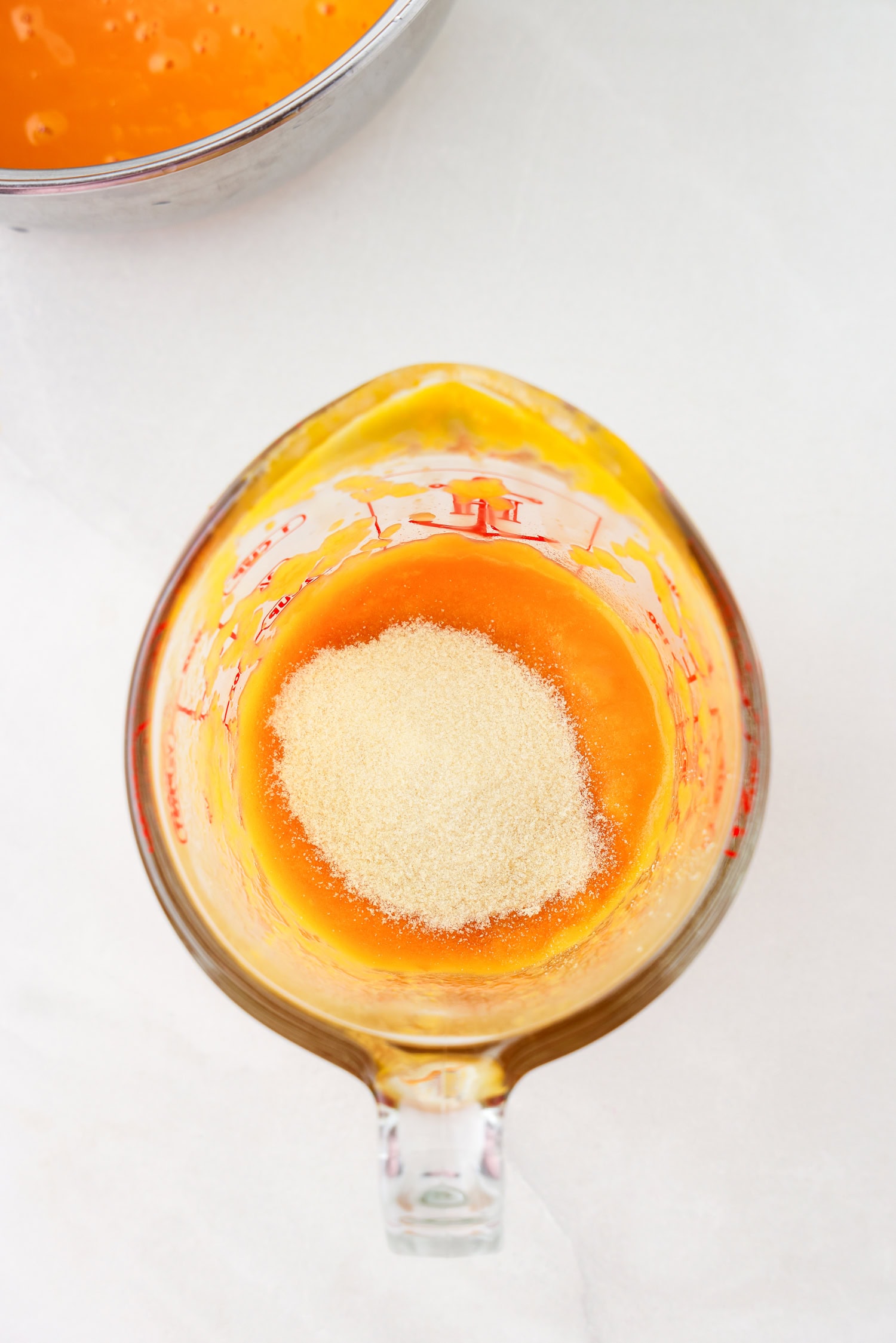 Orange fruit mixture blended in glass measuring cup with gelatin unmixed.