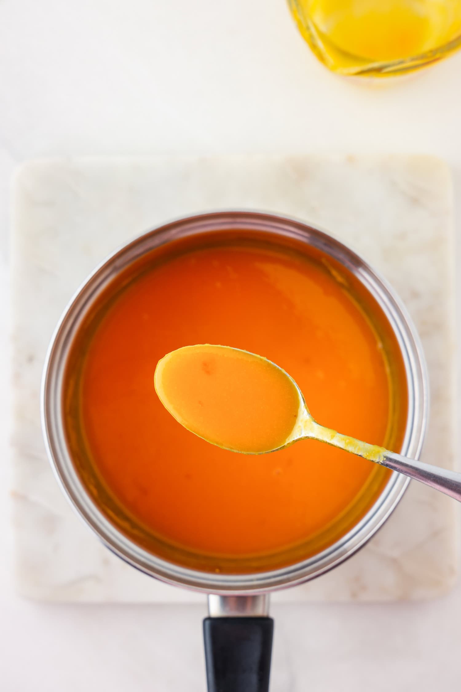 Orange fruit mixture blended in sauce pan with spoon scooping.