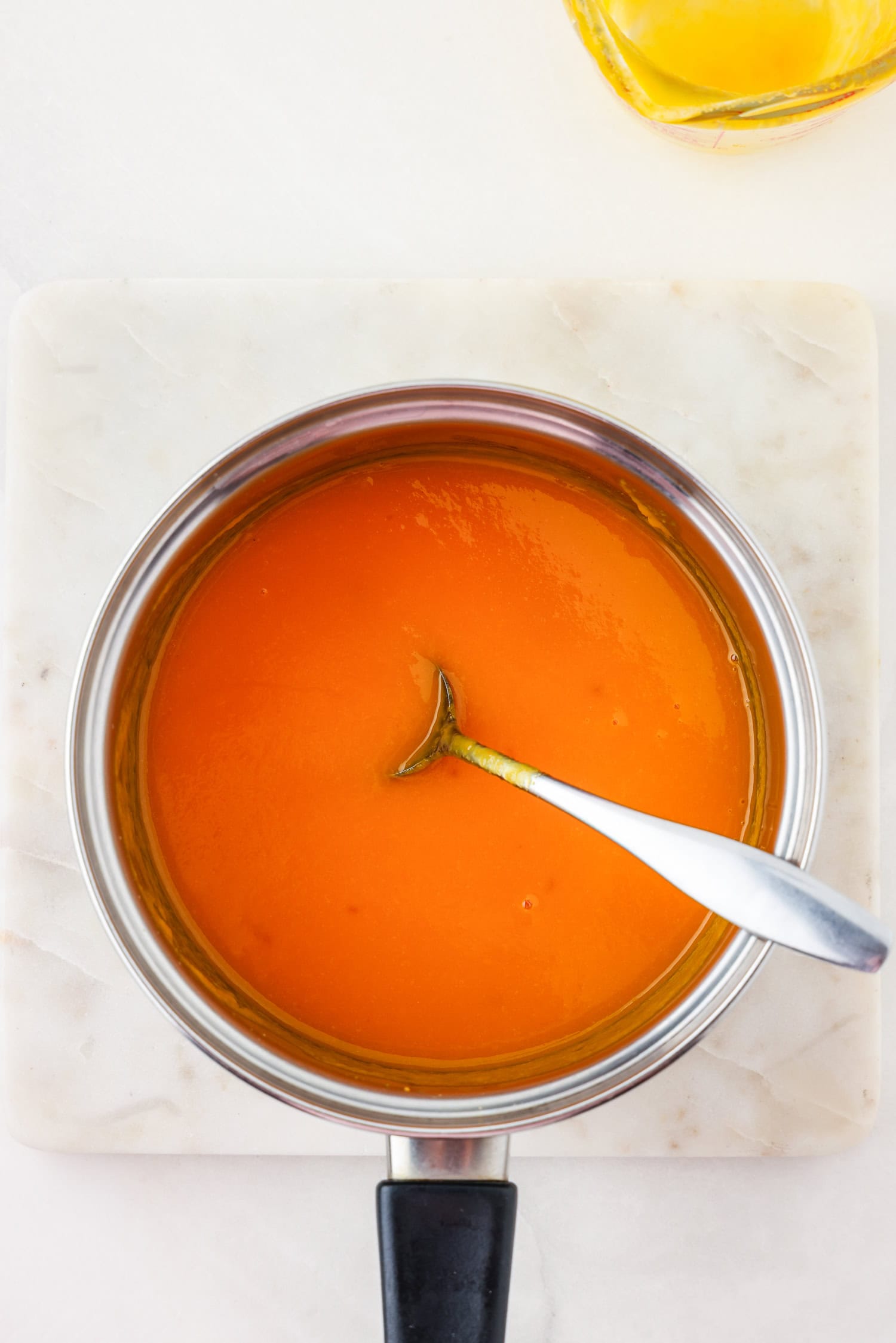 Orange fruit mixture blended in sauce pan with spoon scooping.