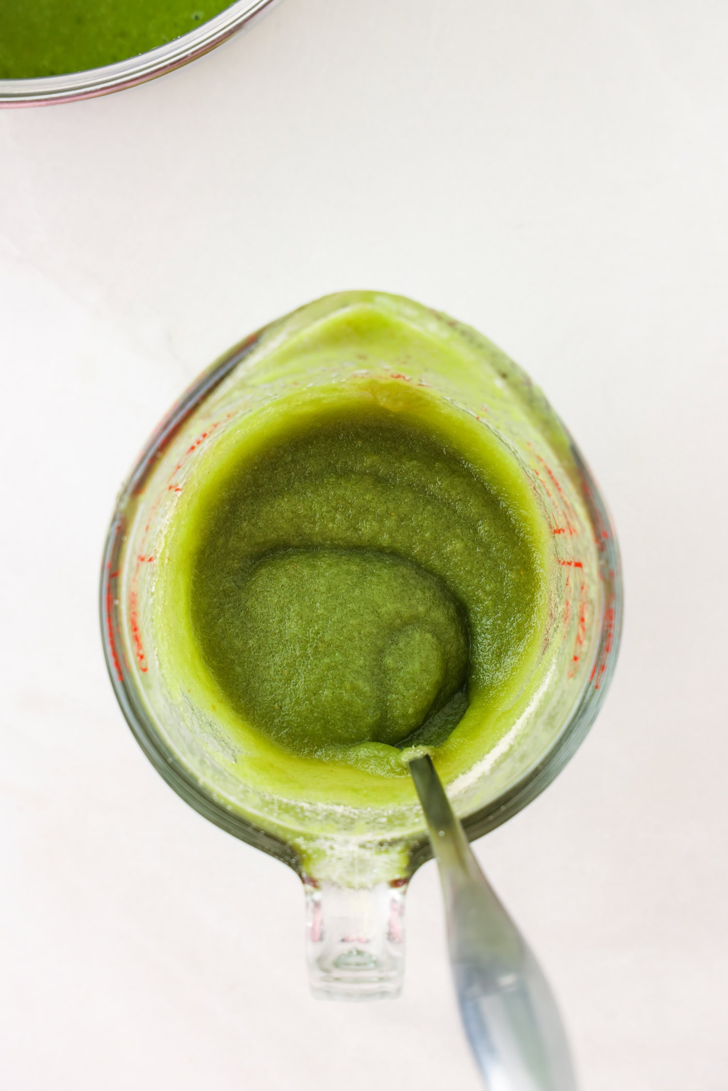 Green fruit mixture blended in a glass measuring cup with gelatin mixed.