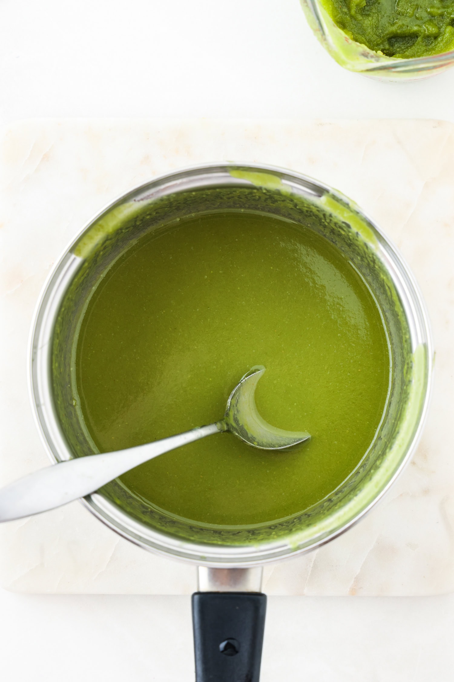 Green fruit mixture blended in a sauce pan with spoon scooping it.