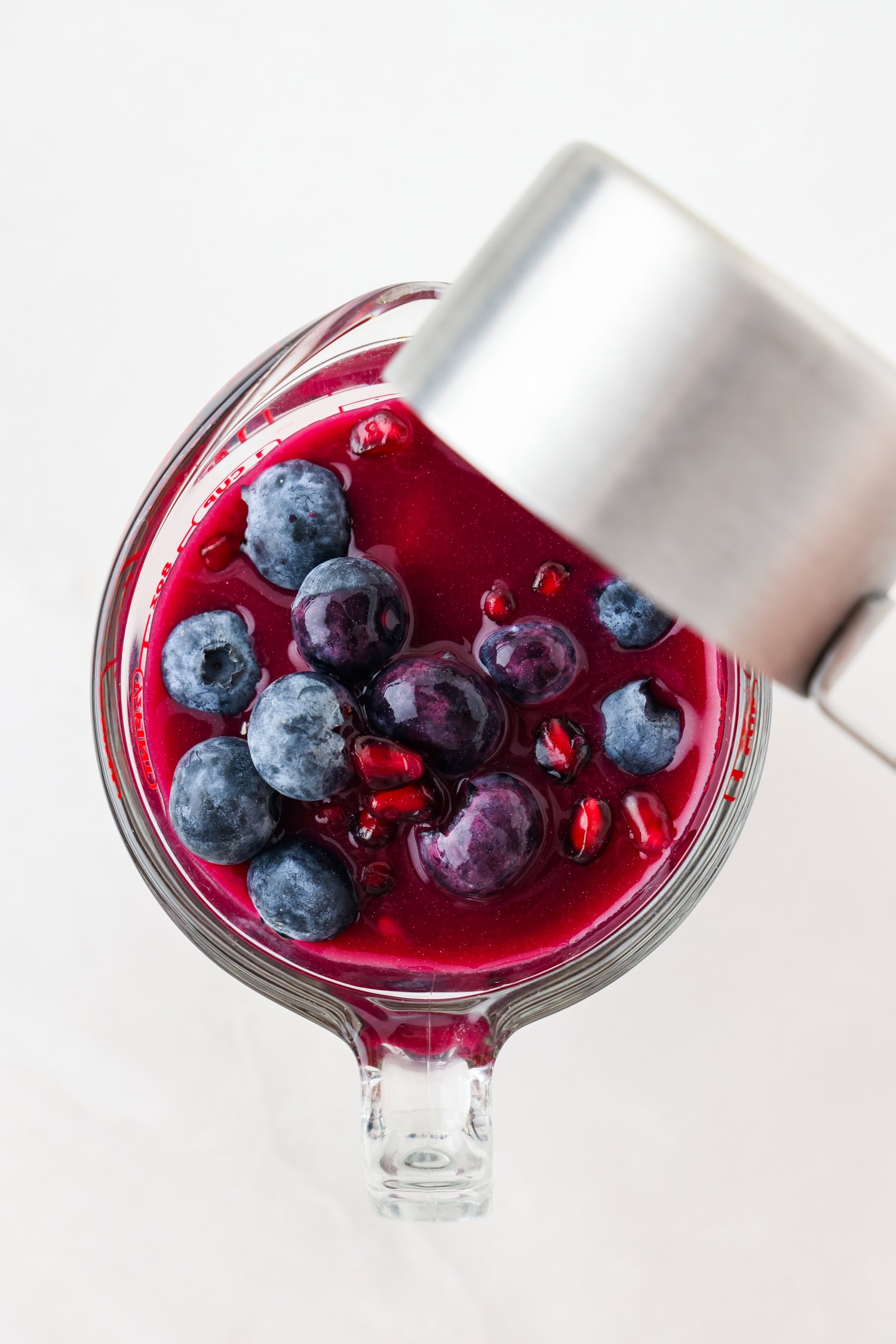 Overhead picture of purple fruit mixture in a measuring glass with liquid ingredients poured on top.