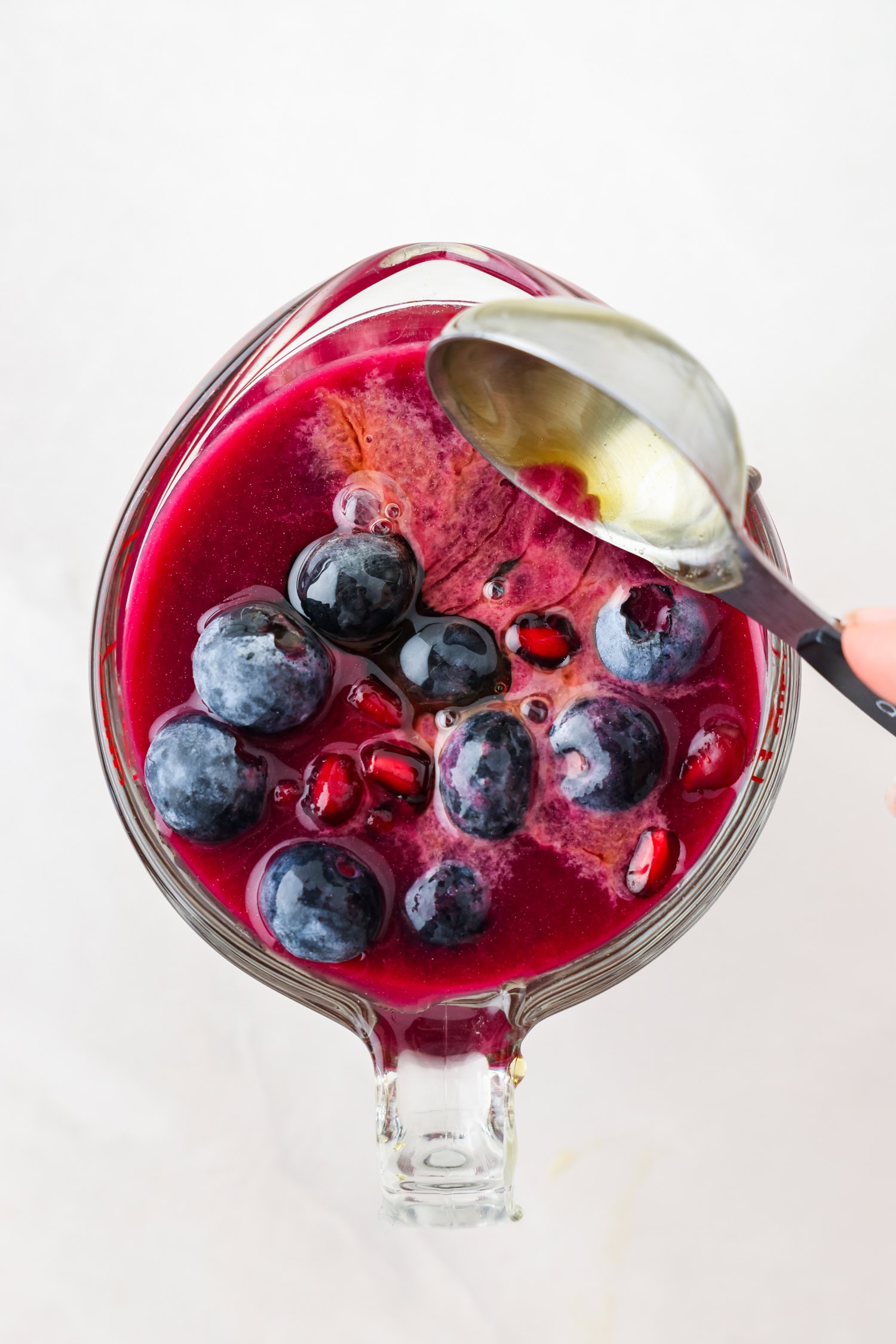 Overhead picture of purple fruit mixture in a measuring glass with liquid ingredients being poured on top
