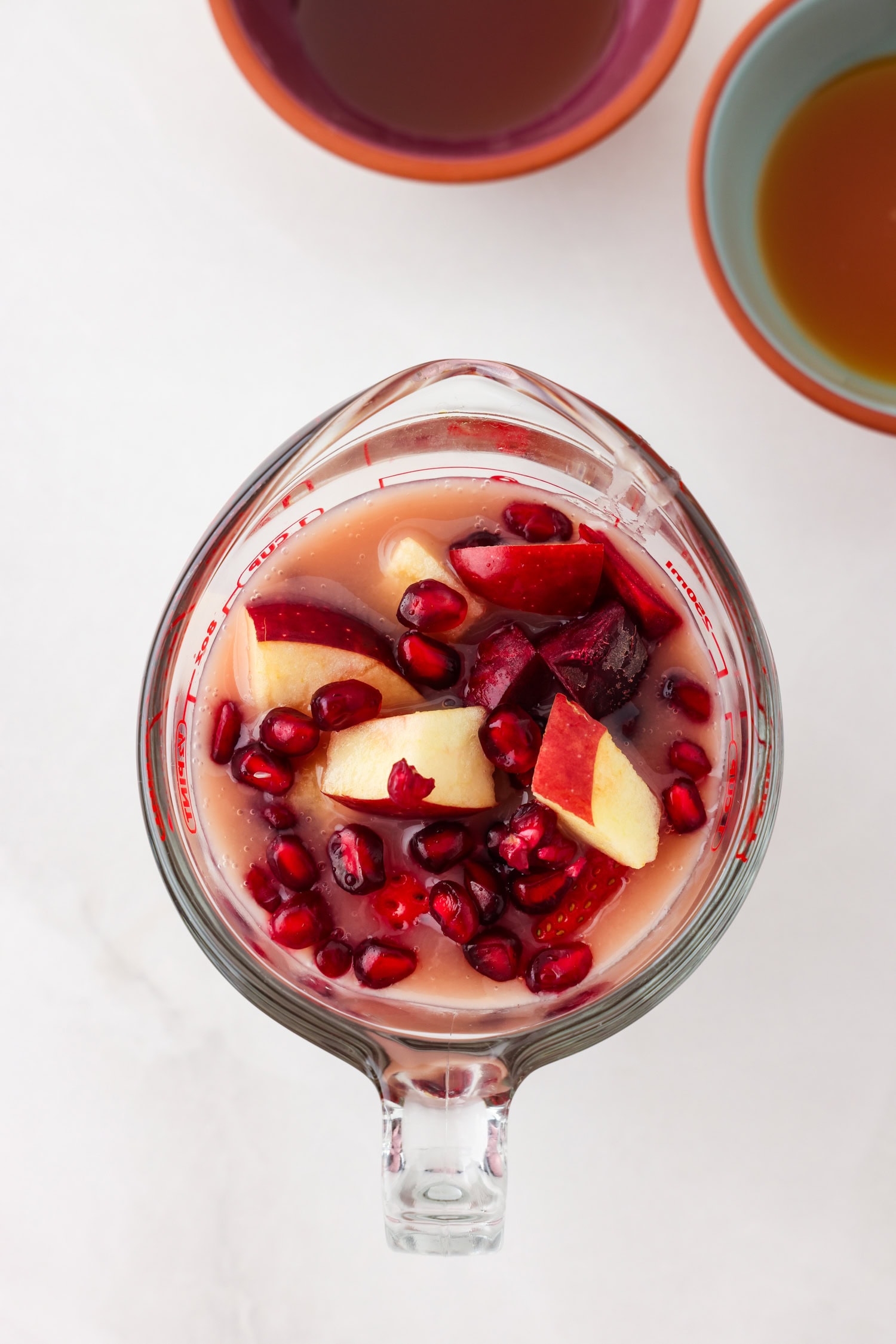 Overhead picture of red fruit mixture in a measuring glass with liquid ingredients poured on top