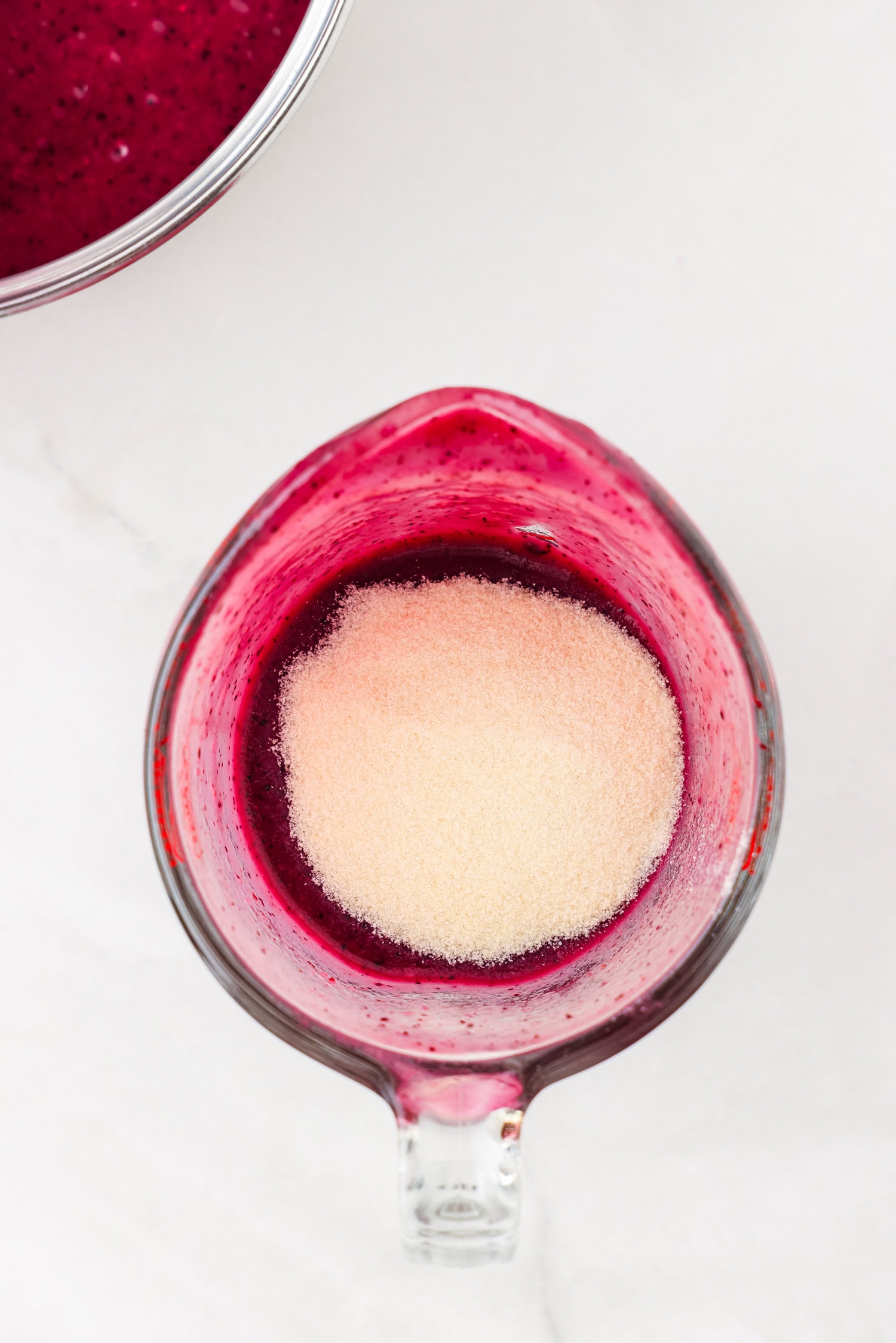 Purple fruit mixture blended in a glass measuring cup with gelatin poured in unmixed.