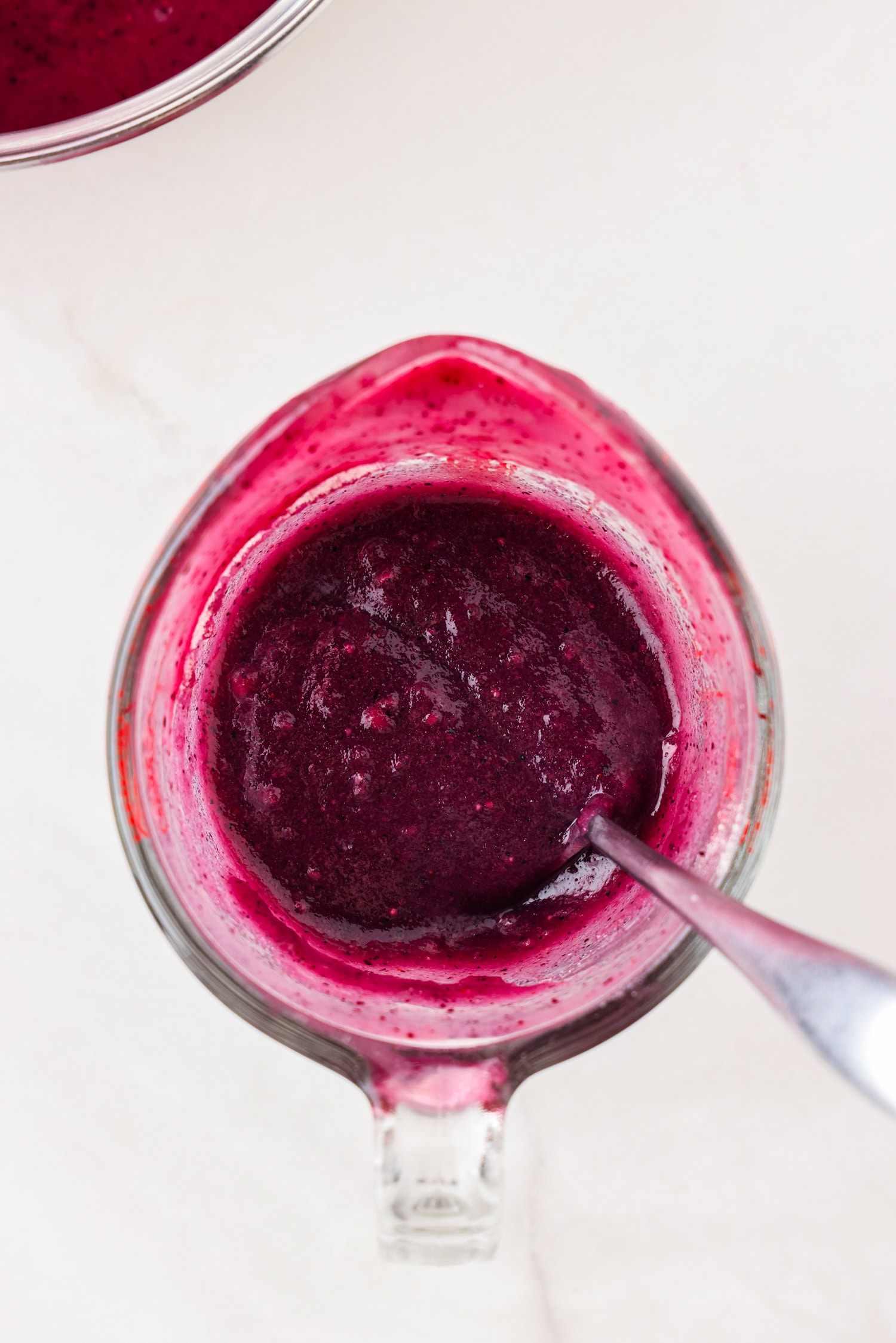 Purple fruit mixture blended in a glass measuring cup with gelatin poured in mixed.