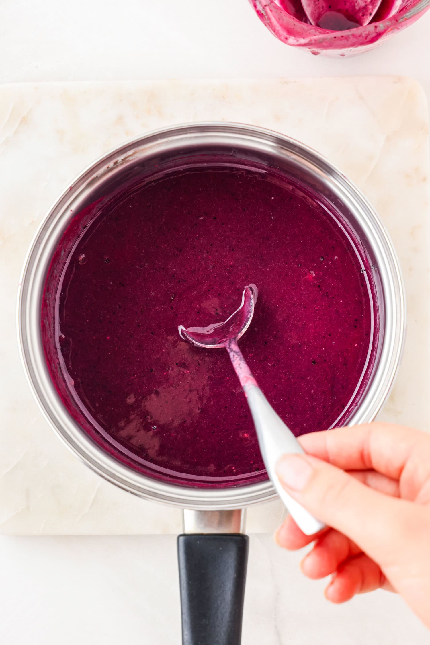 Purple fruit ingredients in a sauce pan with a spoon scooping it.