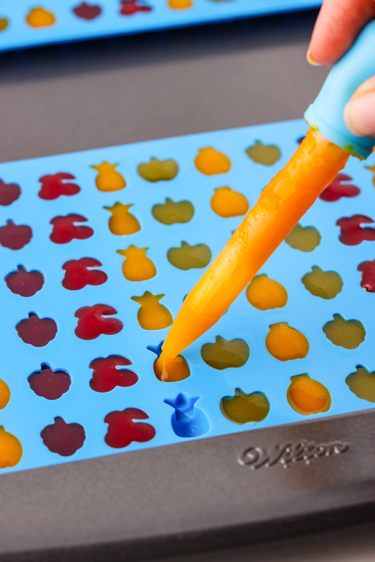 Dropper putting orange fruit mixture into fruit snack molds.