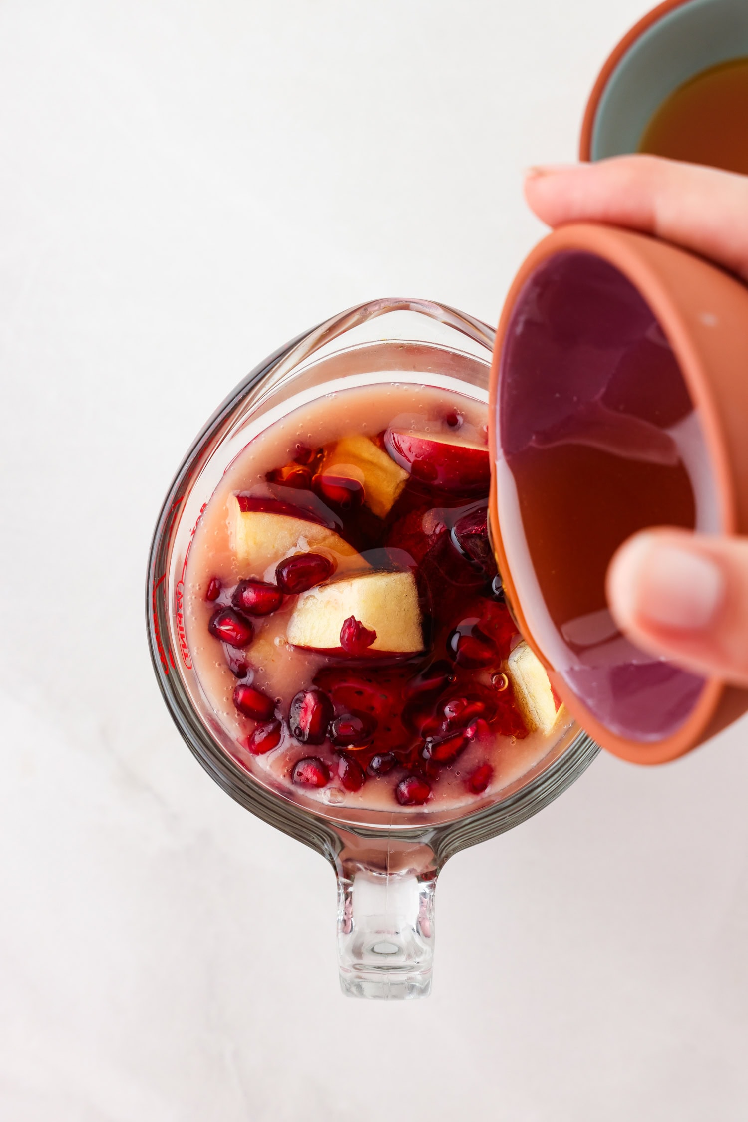 Overhead picture of red fruit mixture in a measuring glass with liquid honey being poured on top.
