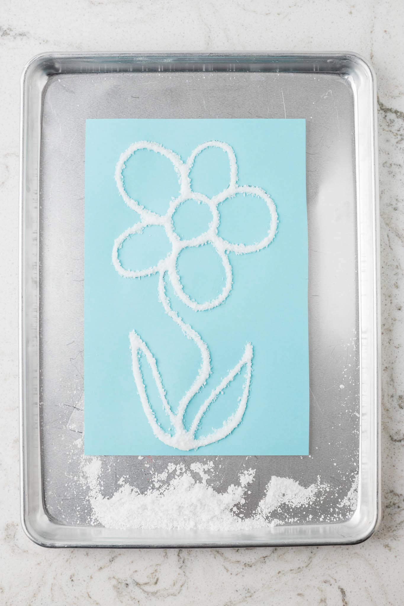 The excess salt has been shaken off, leaving a crisp, raised, salt-covered outline of the flower on the blue paper.